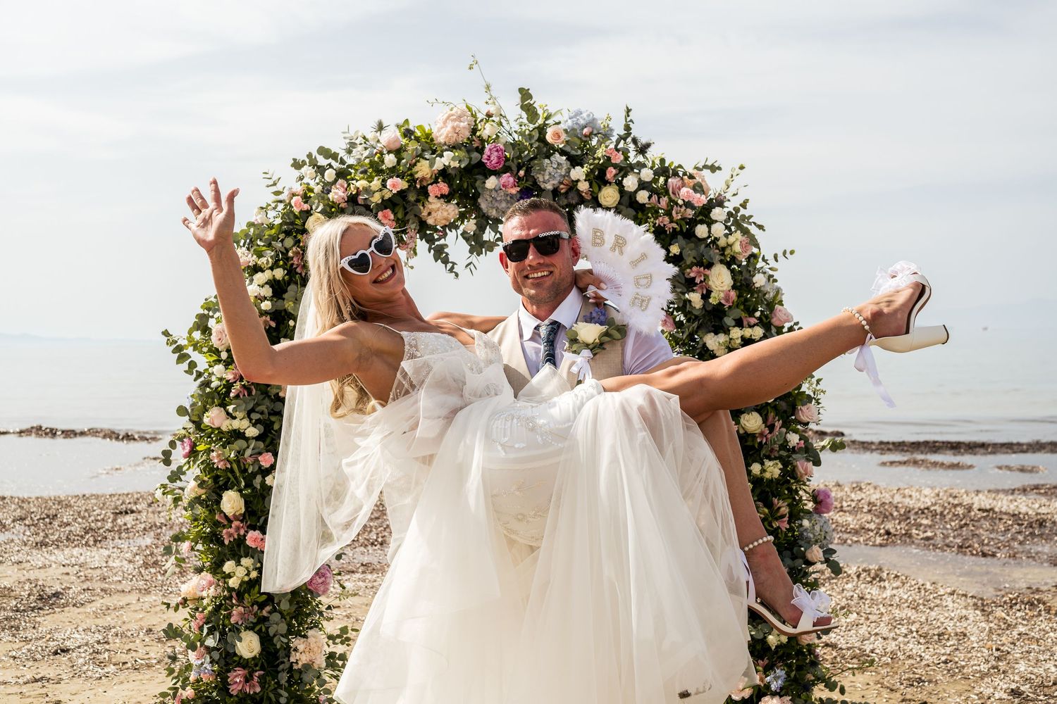 Celebratory moment under a floral arch at a beach wedding.