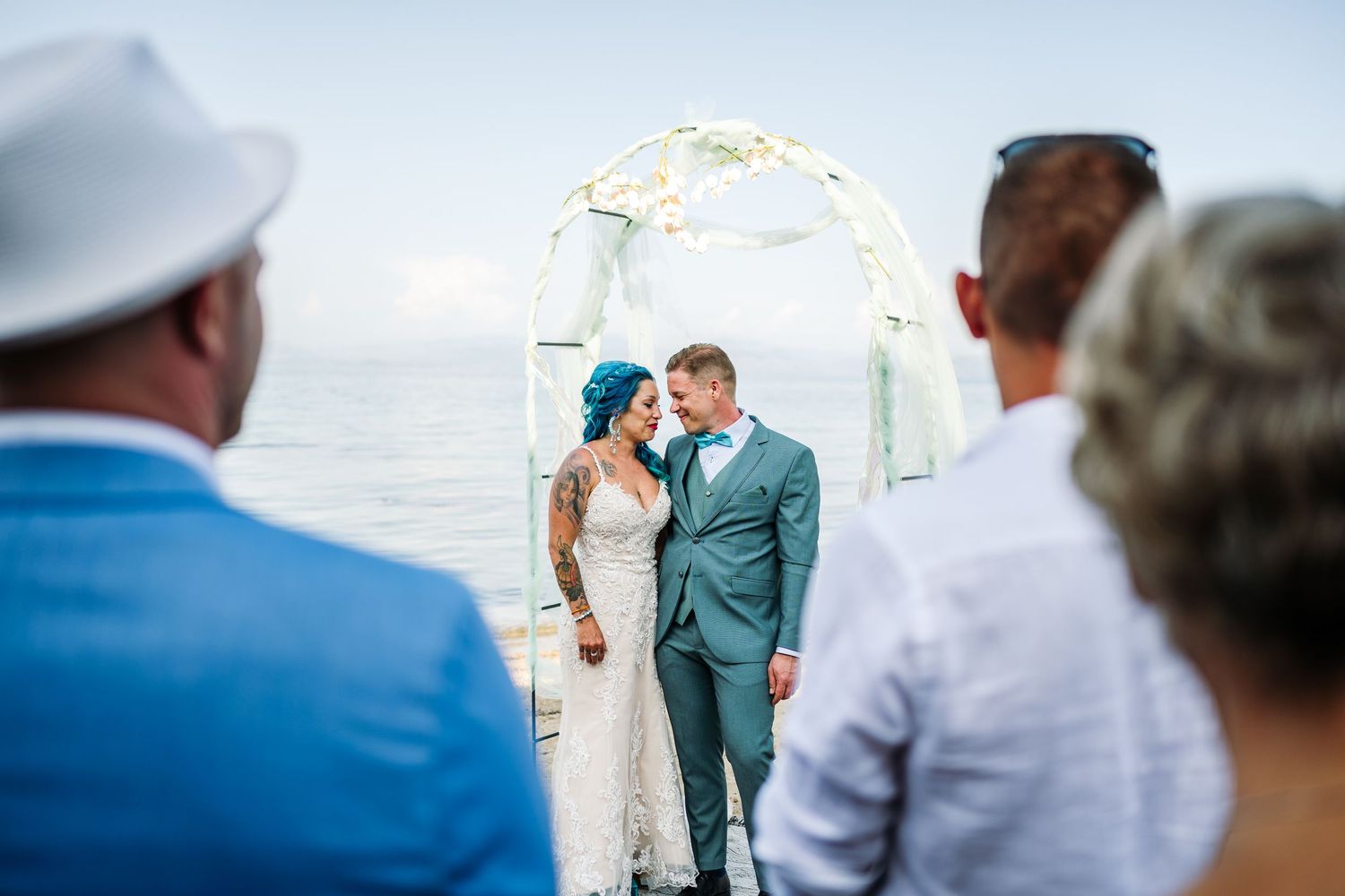 Beach wedding ceremony setup with guests watching under blue skies.