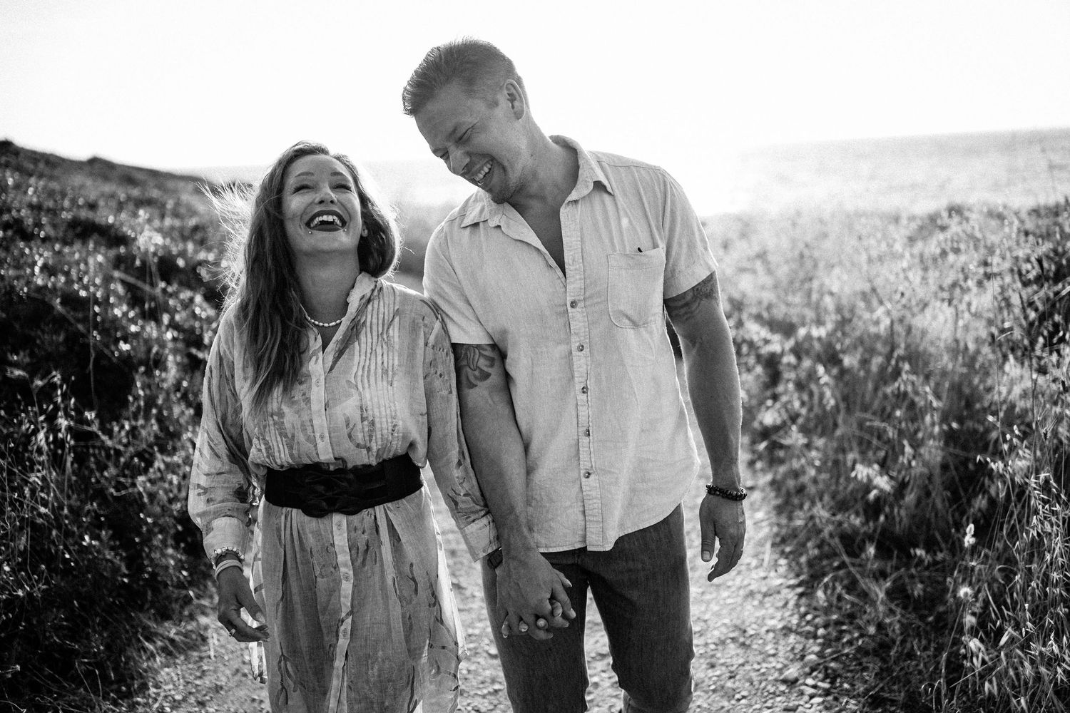 A couple shares laughter while walking through a scenic coastal landscape.