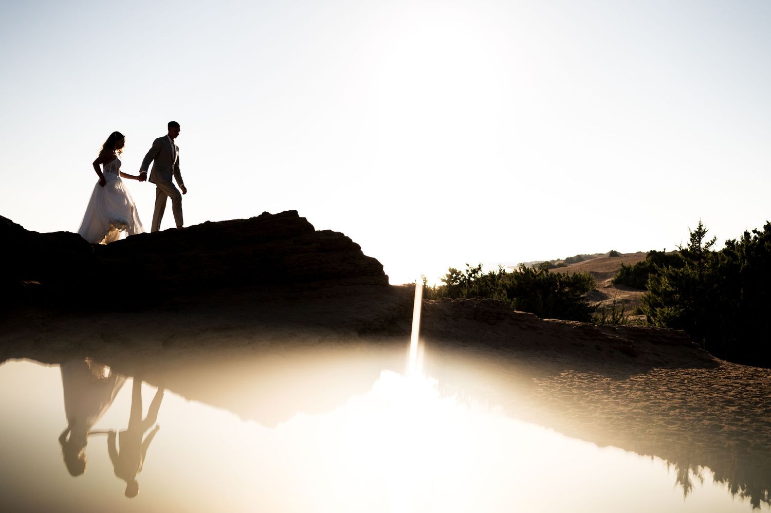 Silhouetted figures against bright sunlight reflecting on calm water.