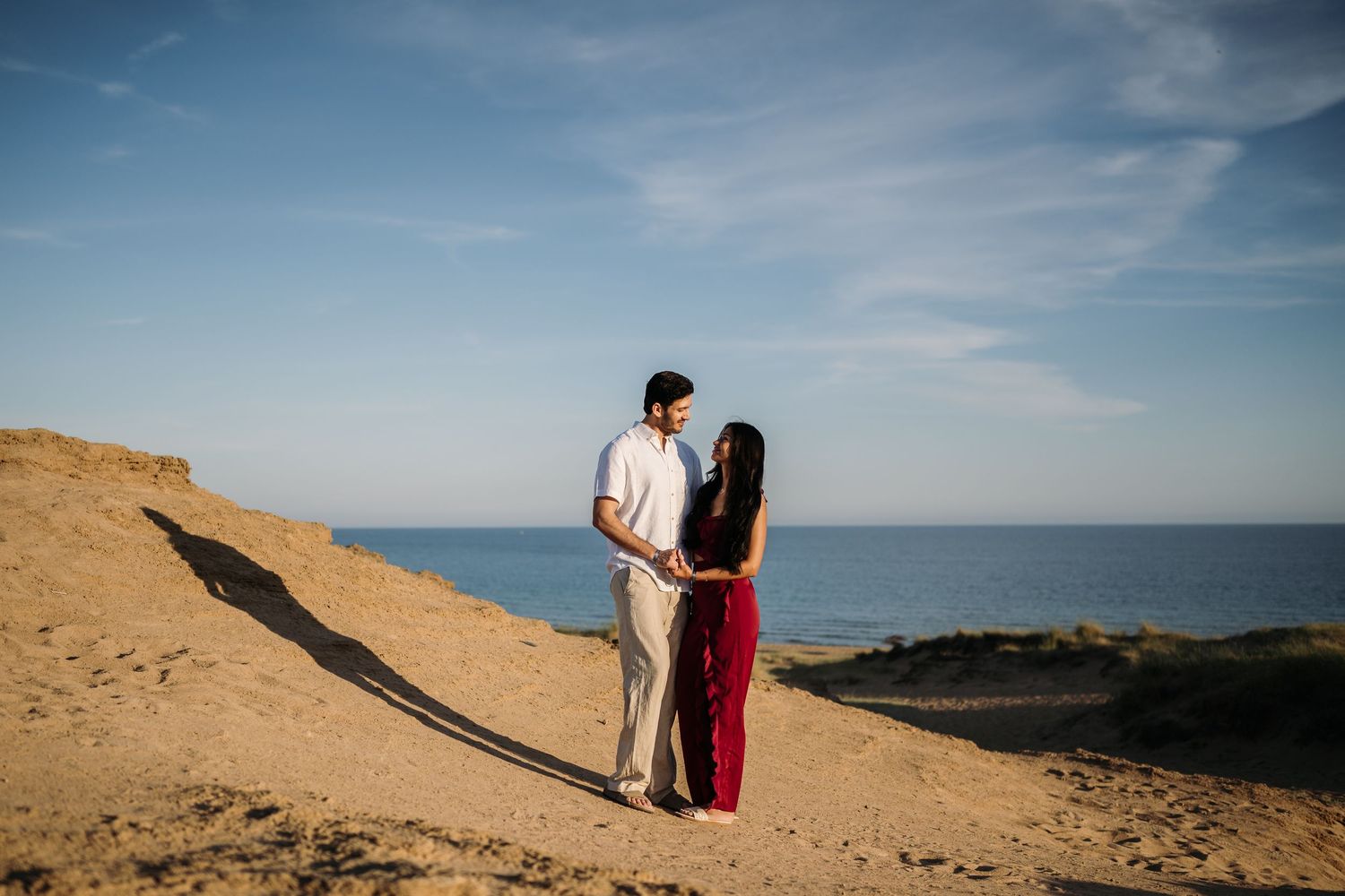A couple standing on coastal cliffs overlooking the ocean during their engagement session.