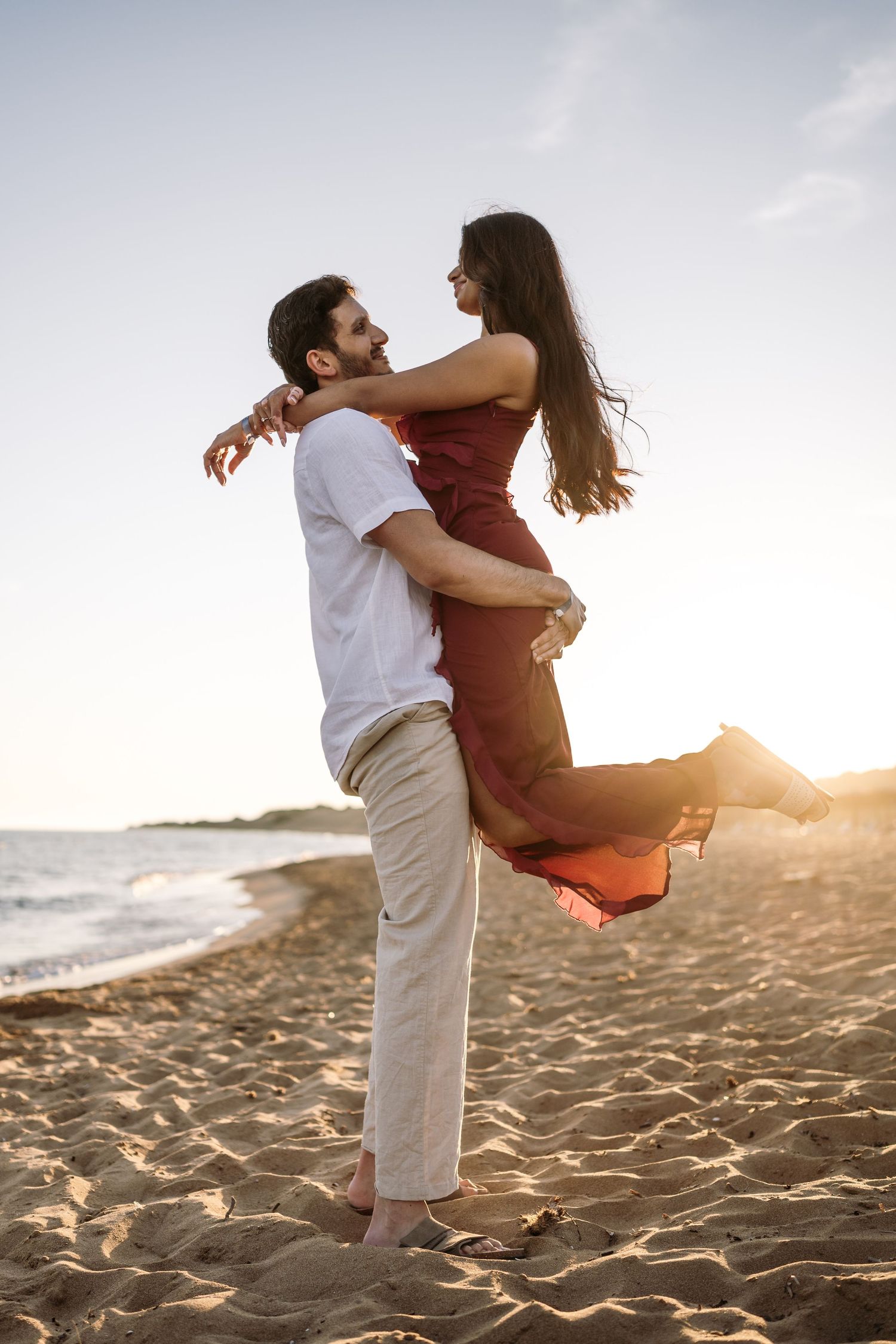 Playful couple embracing and spinning on a sandy beach at sunset.