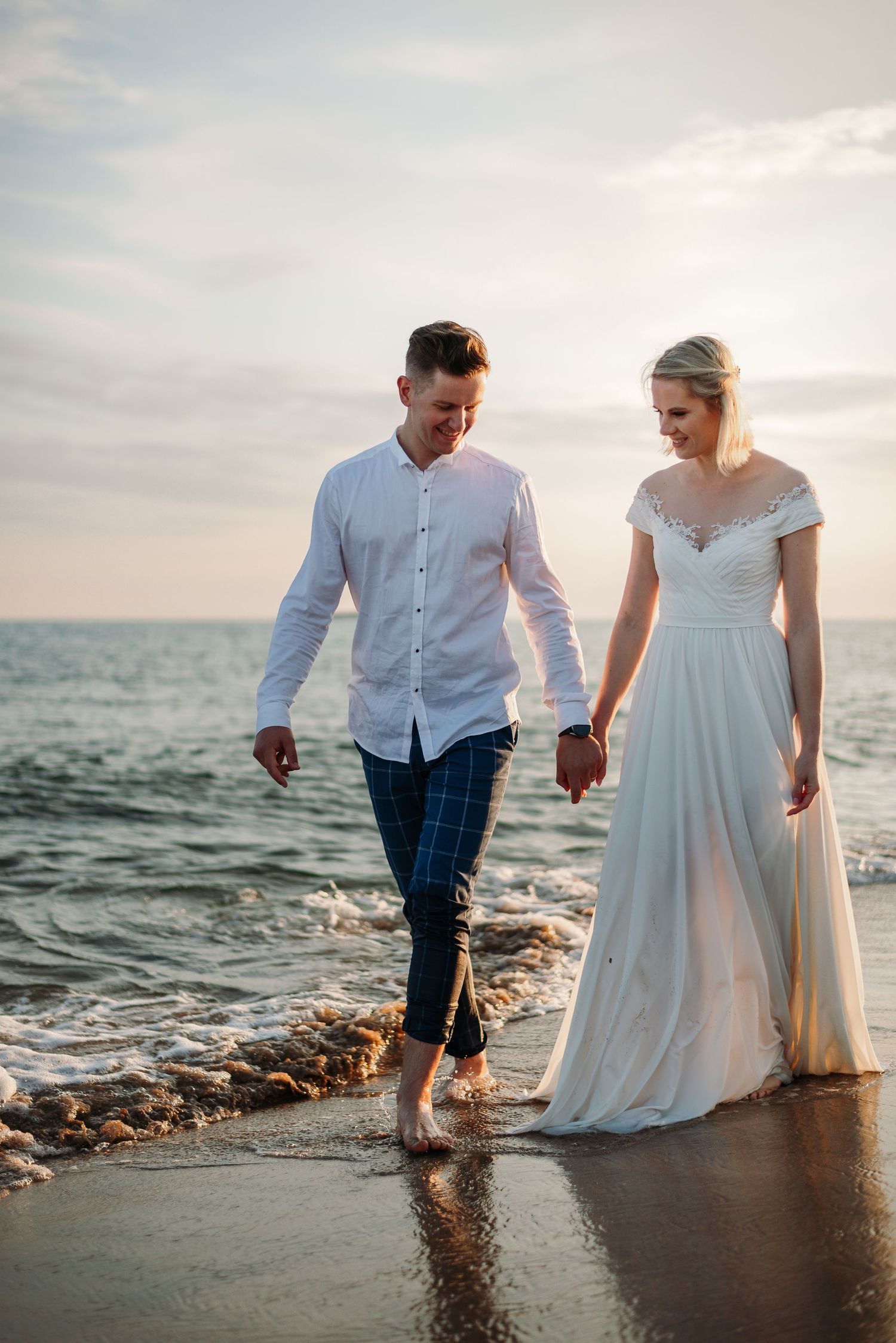 Romantic beach photoshoot with couple walking in waves at golden hour.