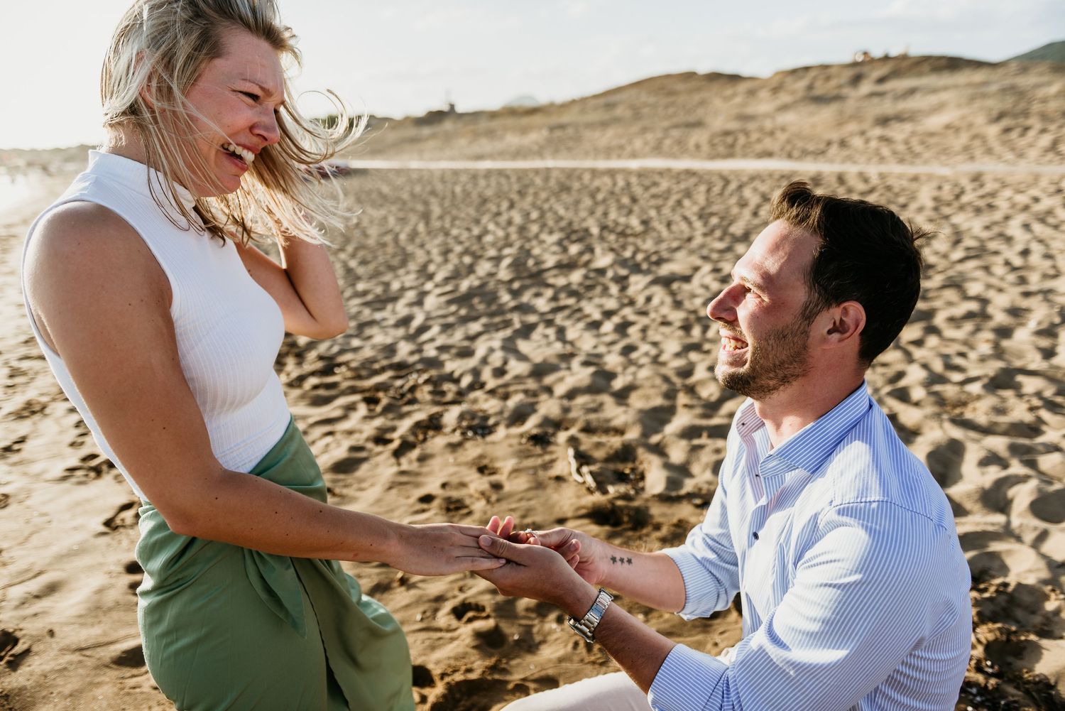 Surprise proposal moment captured on a sandy beach during sunset.