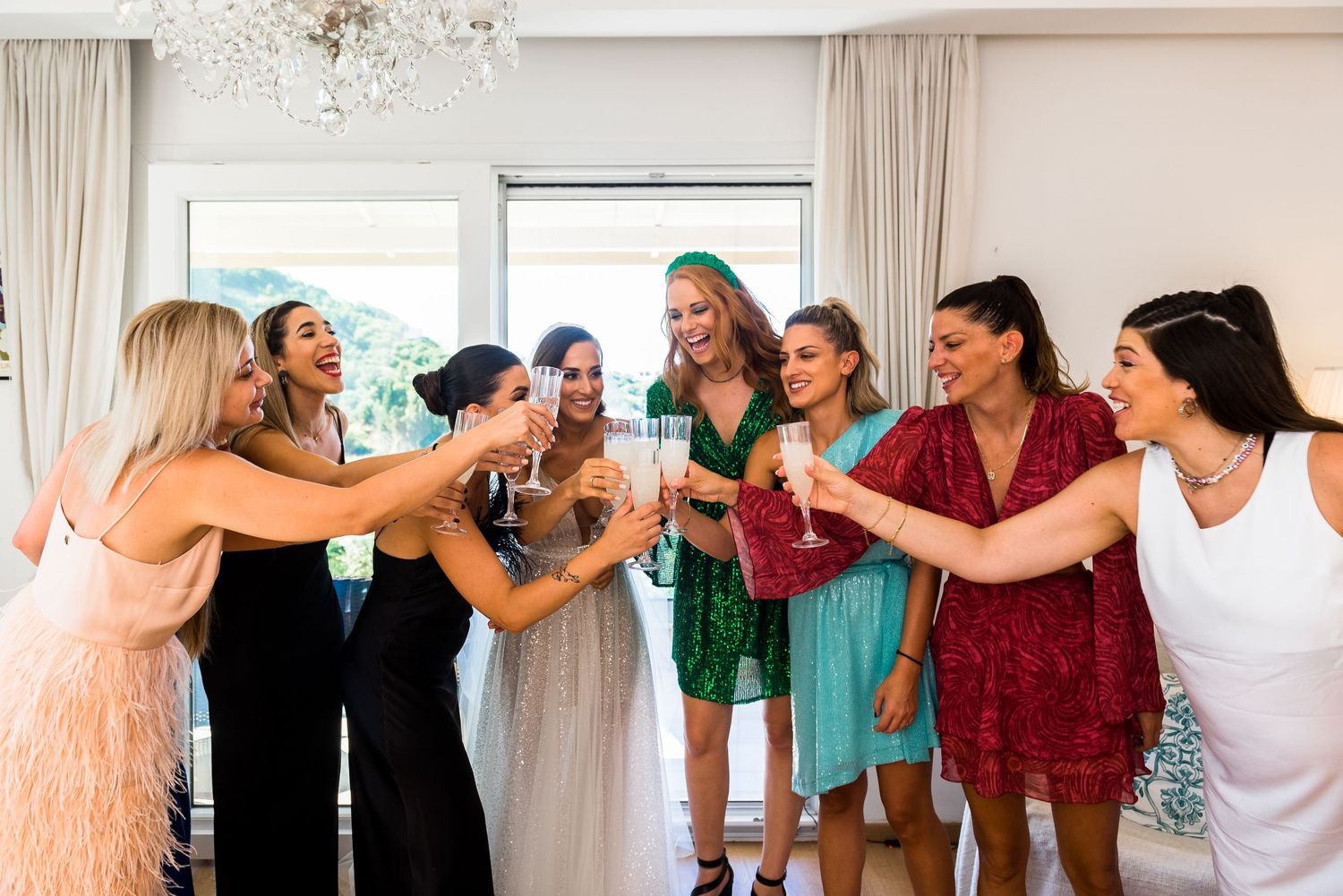 A group of wedding guests stand in a line with arms linked in a bright indoor space.