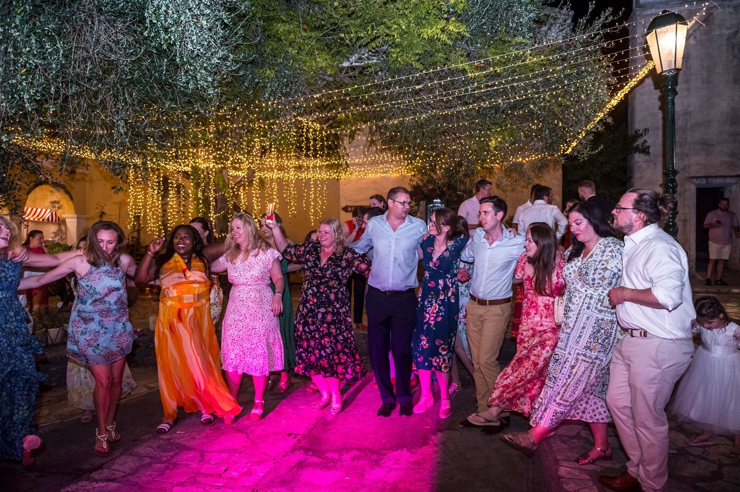 Wedding guests dancing on illuminated dance floor under string lights at outdoor reception.