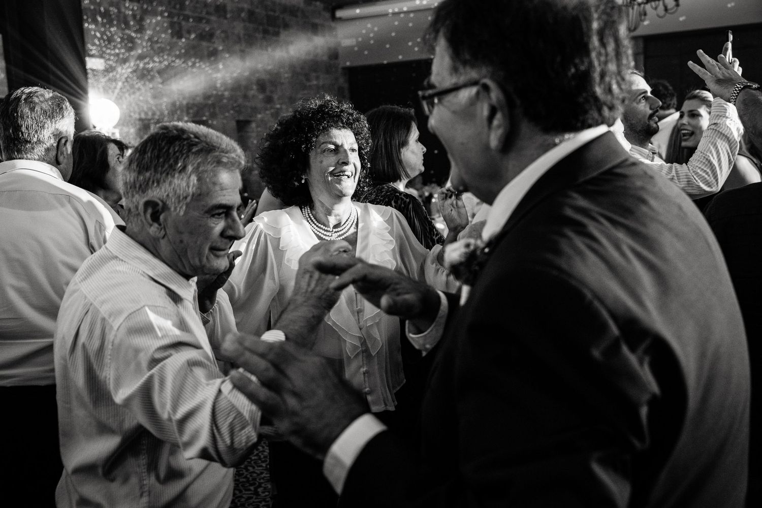 Black and white photo of wedding guests dancing and celebrating at an indoor reception.