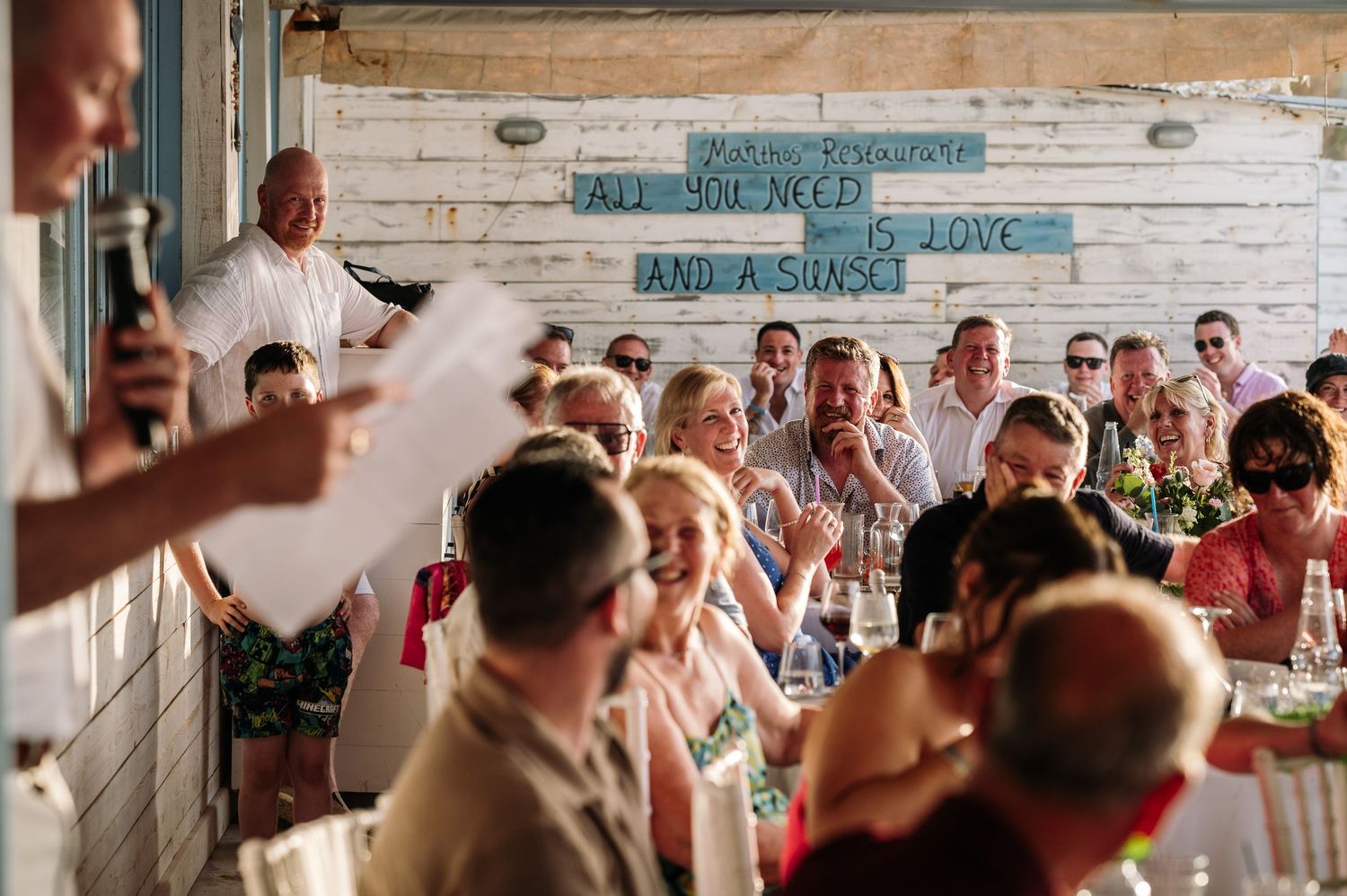 Wedding celebration under rustic wooden beams with vintage coastal decor and dancing guests.