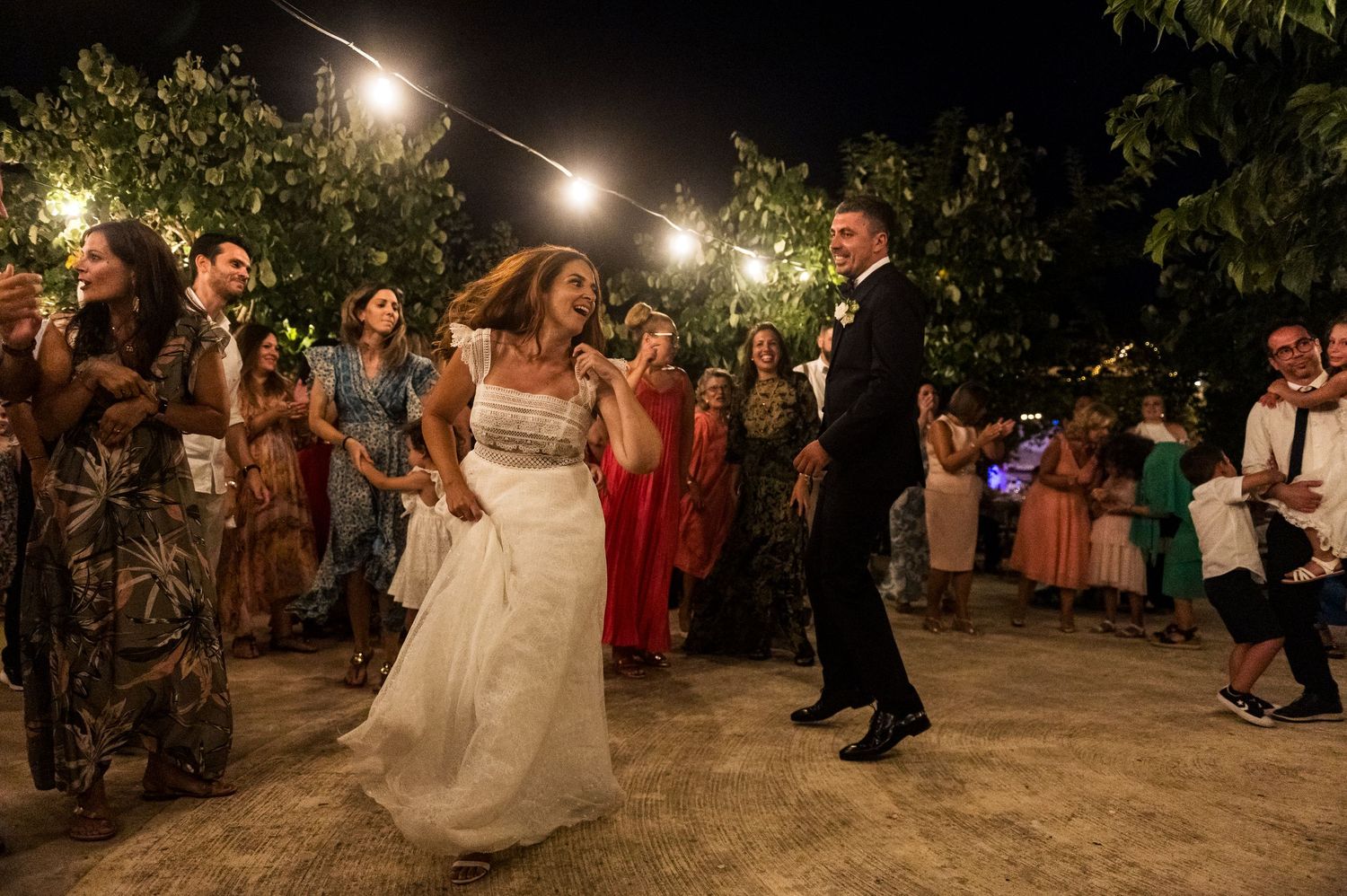 A wedding reception dance under string lights with guests watching in an outdoor garden setting.