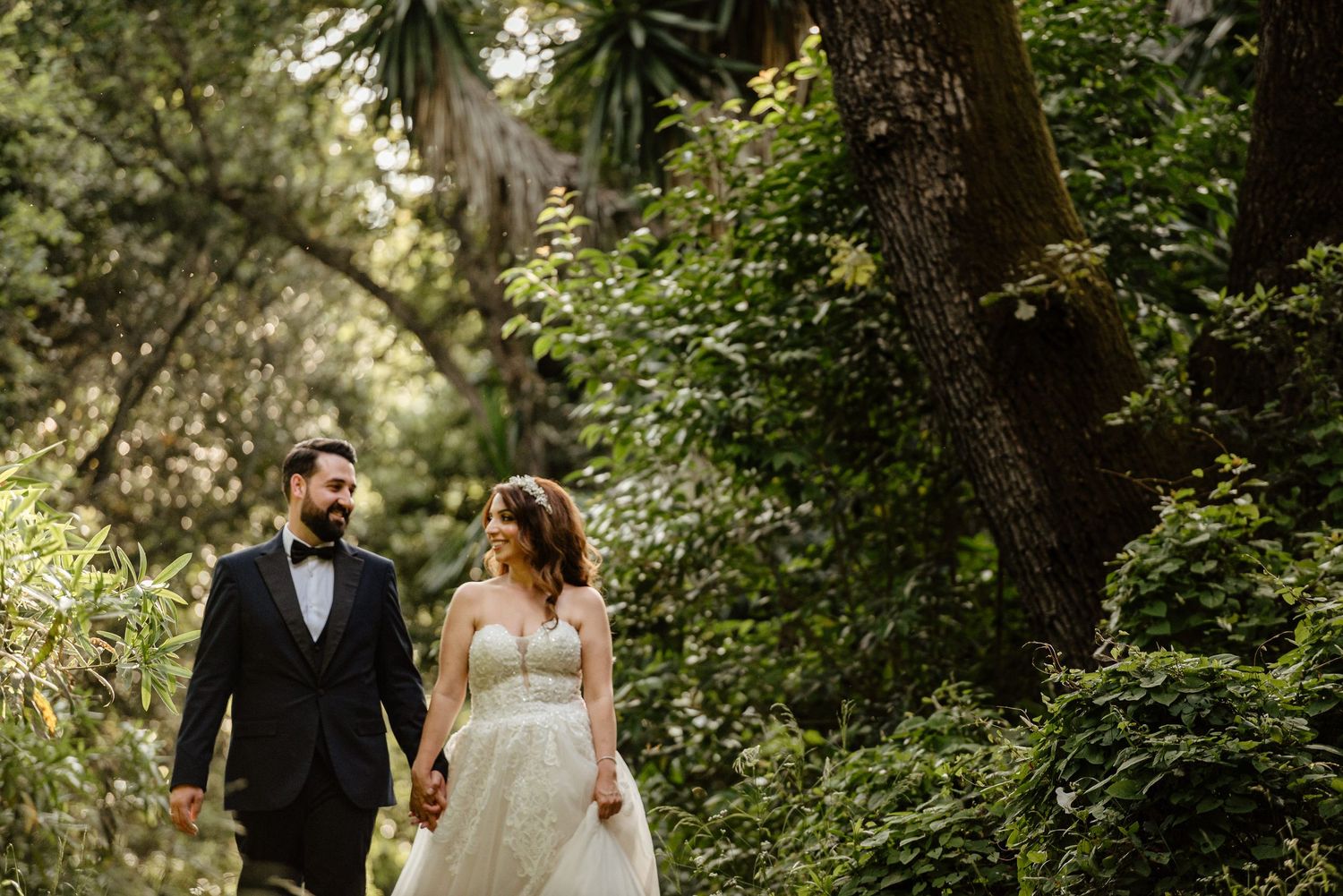 Wedding couple walks through a lush garden path surrounded by greenery.