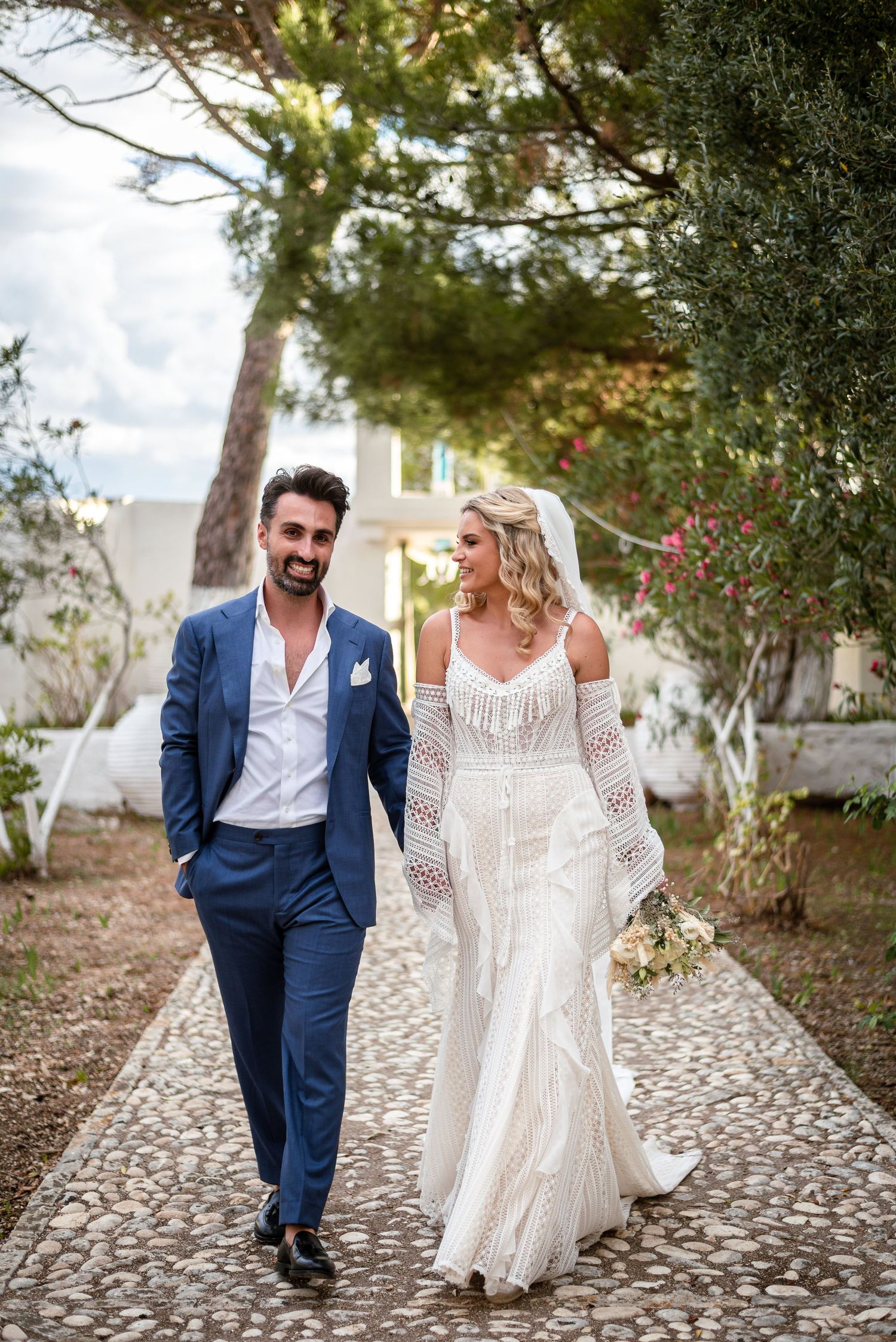 Couple walking along stone pathway surrounded by lush greenery.