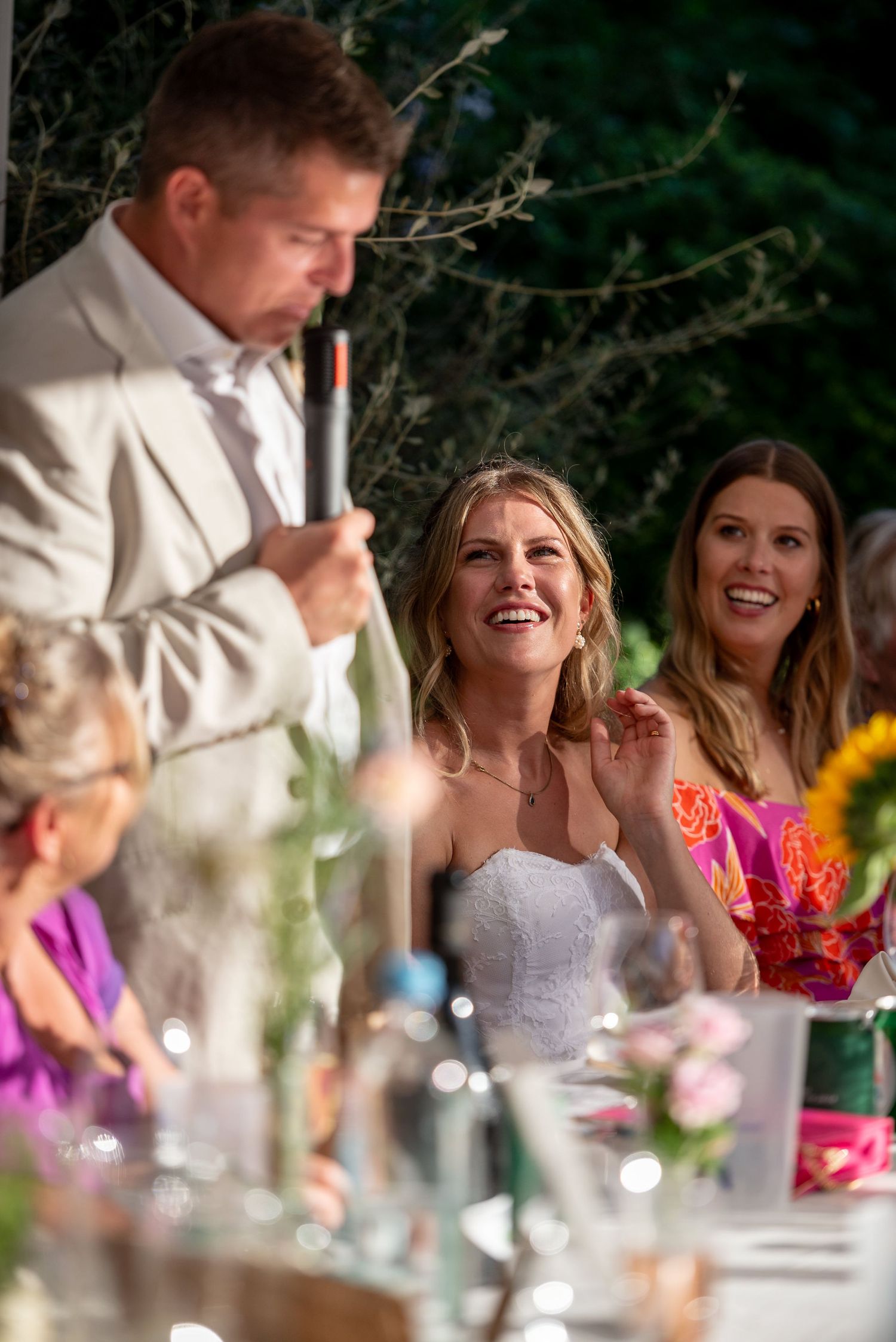 Wedding reception guests sharing laughter during dinner under outdoor tent lighting.
