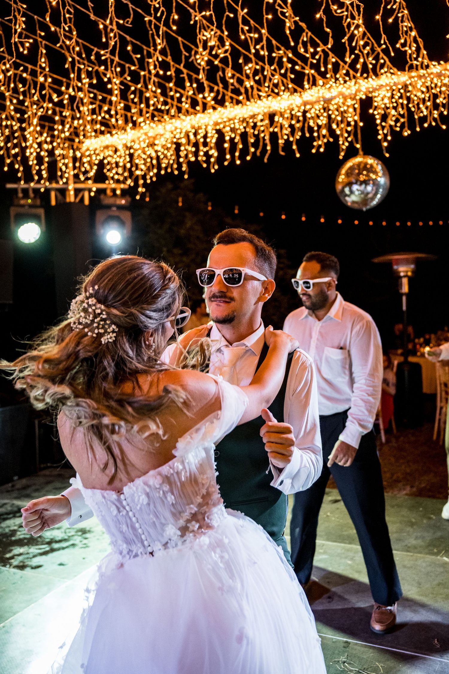 Wedding reception dance floor with guests celebrating under warm fairy light canopy.