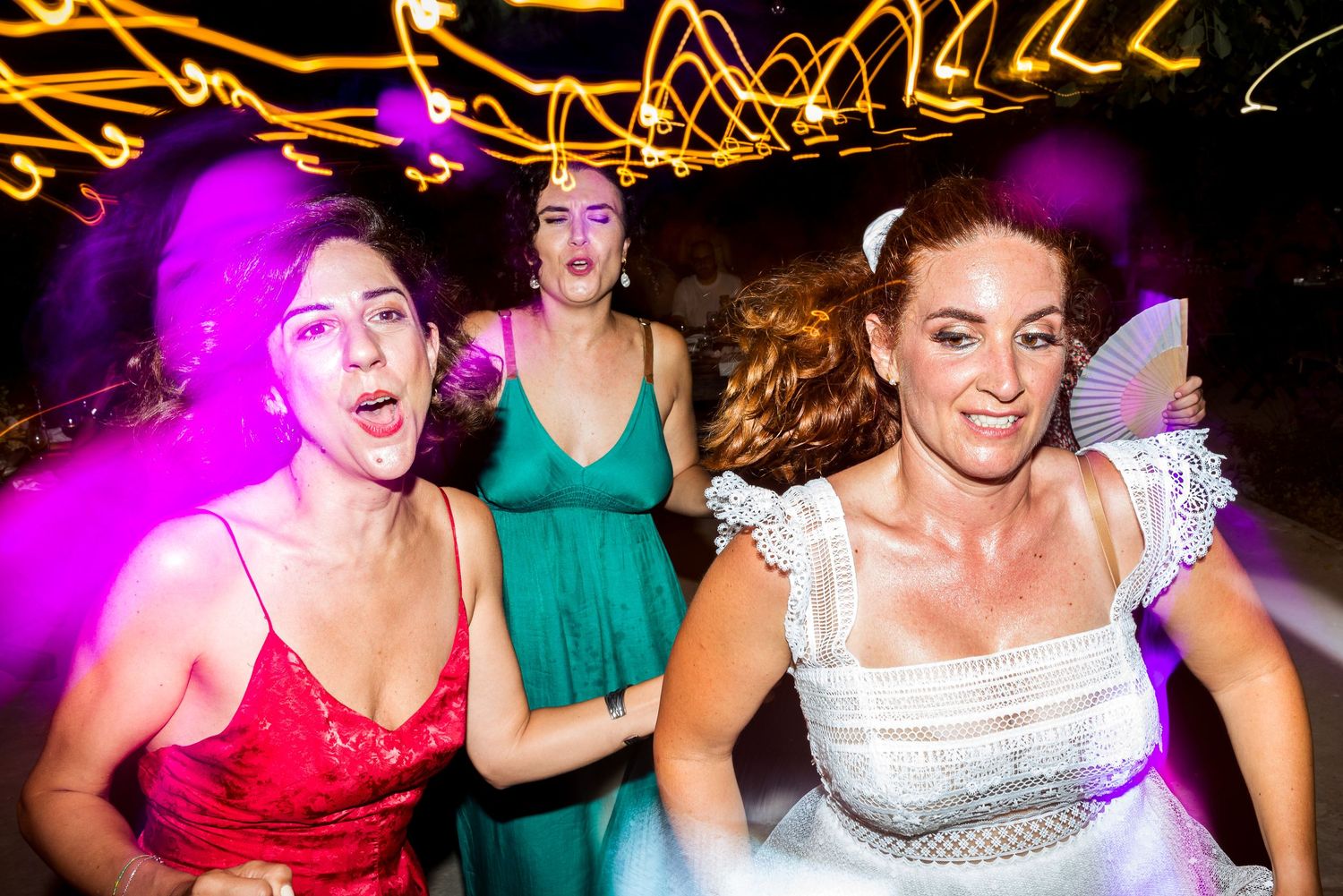 Colorful lighting creates vibrant atmosphere as wedding guests dance at outdoor reception.