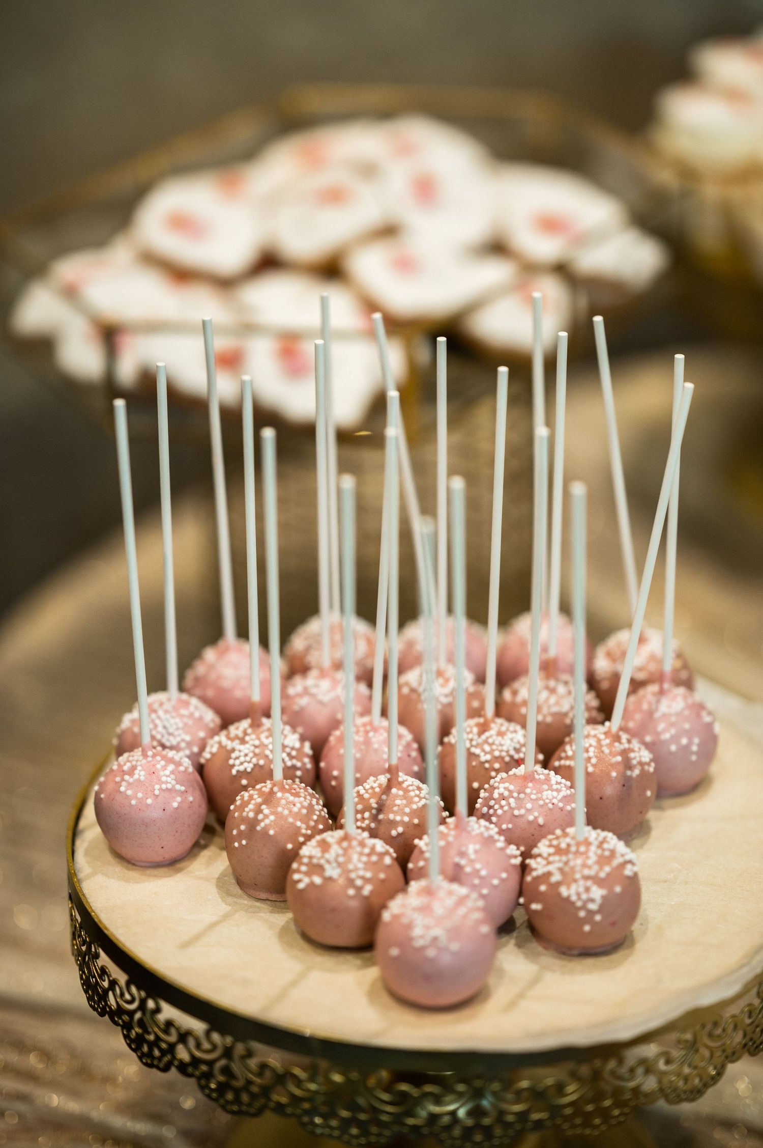 Pink cake pops decorated with white sprinkles displayed on an elegant wooden board.