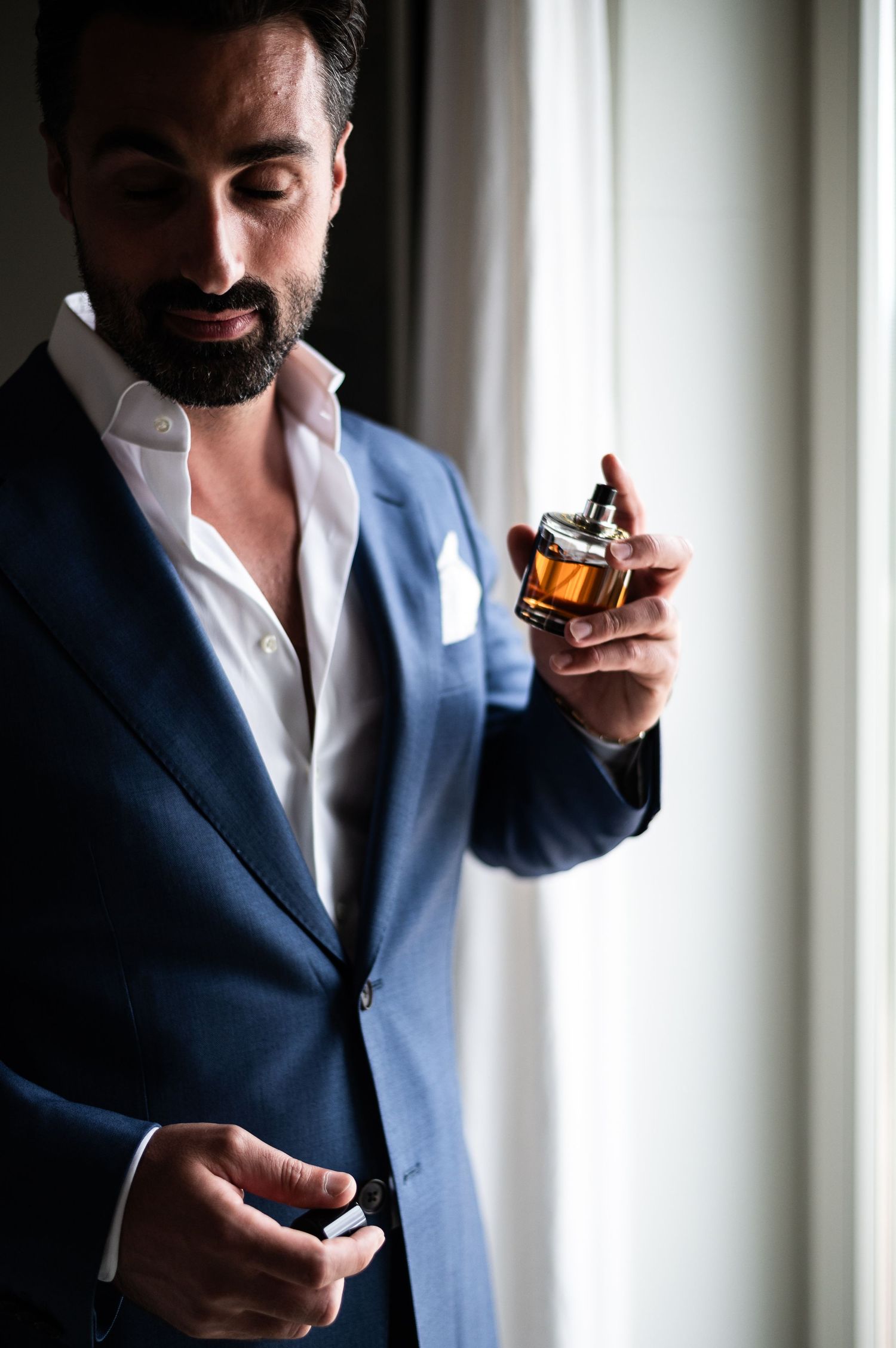 Person in blue blazer applies cologne in artistic getting ready shots.