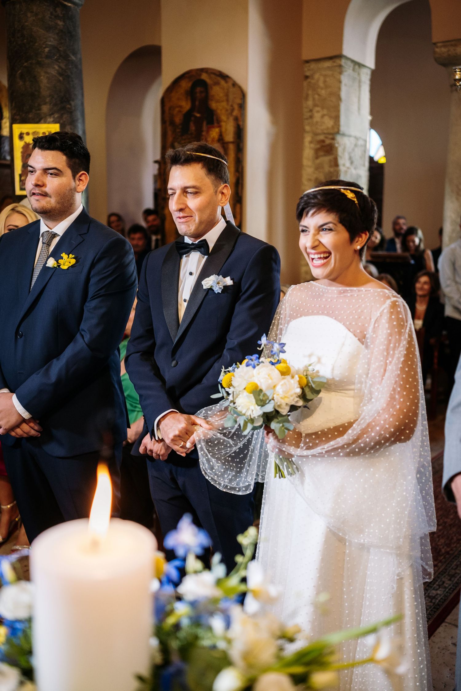 Wedding party standing in a row at an ornate church ceremony with white candles and floral arrangements.