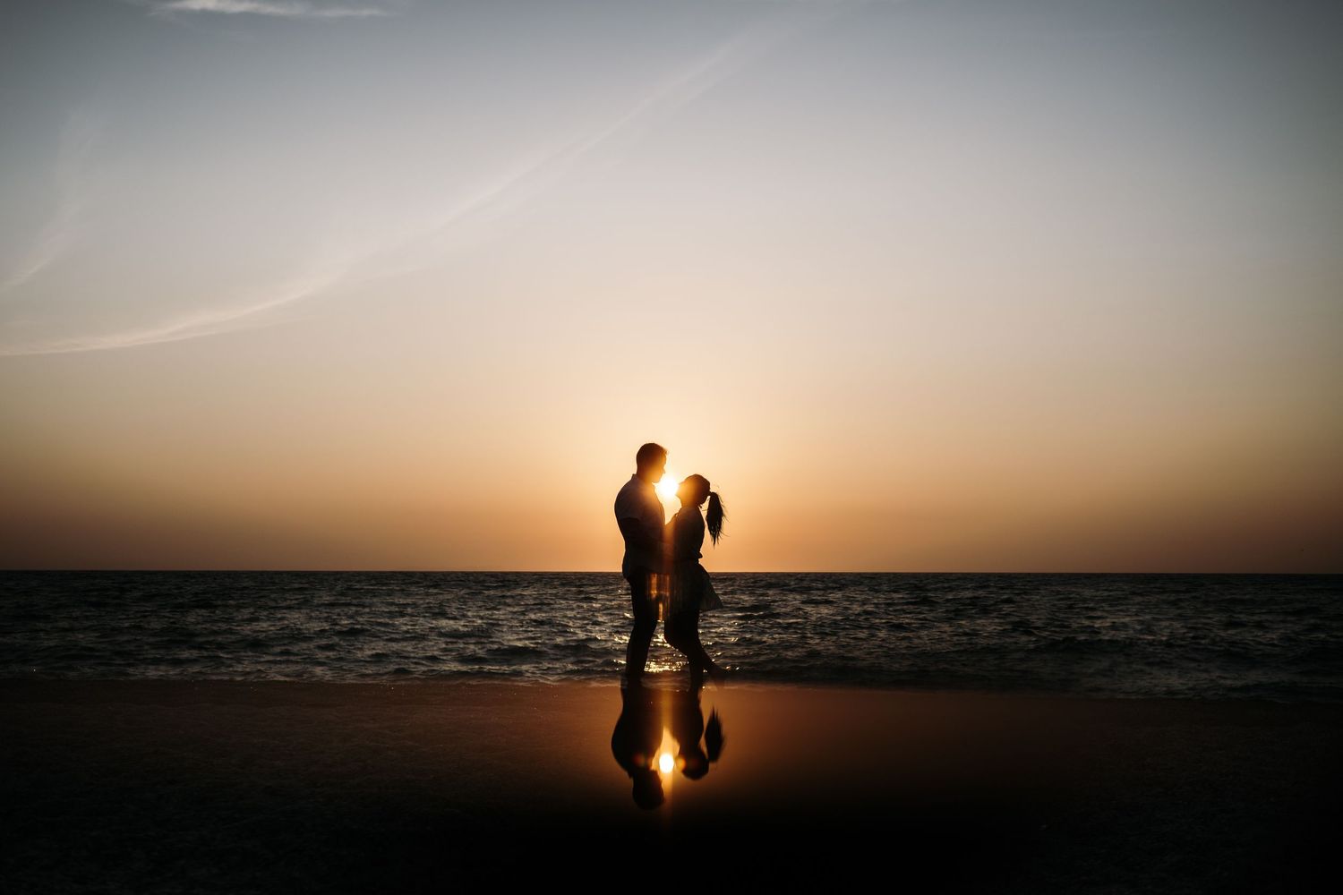 Silhouettes of a couple against a dramatic sunset on the beach.