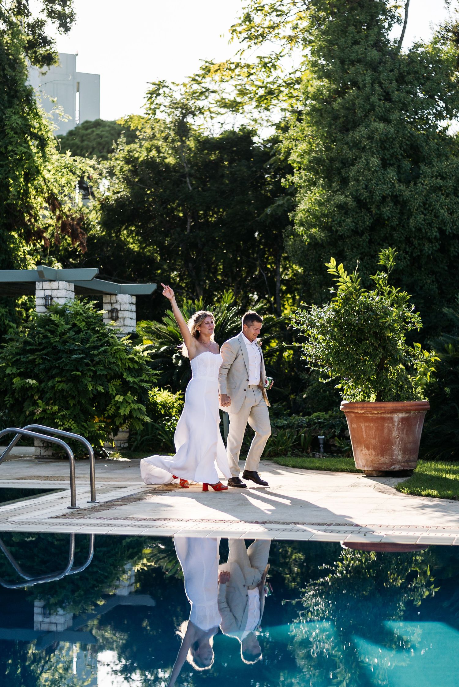 Wedding celebration by a swimming pool surrounded by lush greenery and trees.