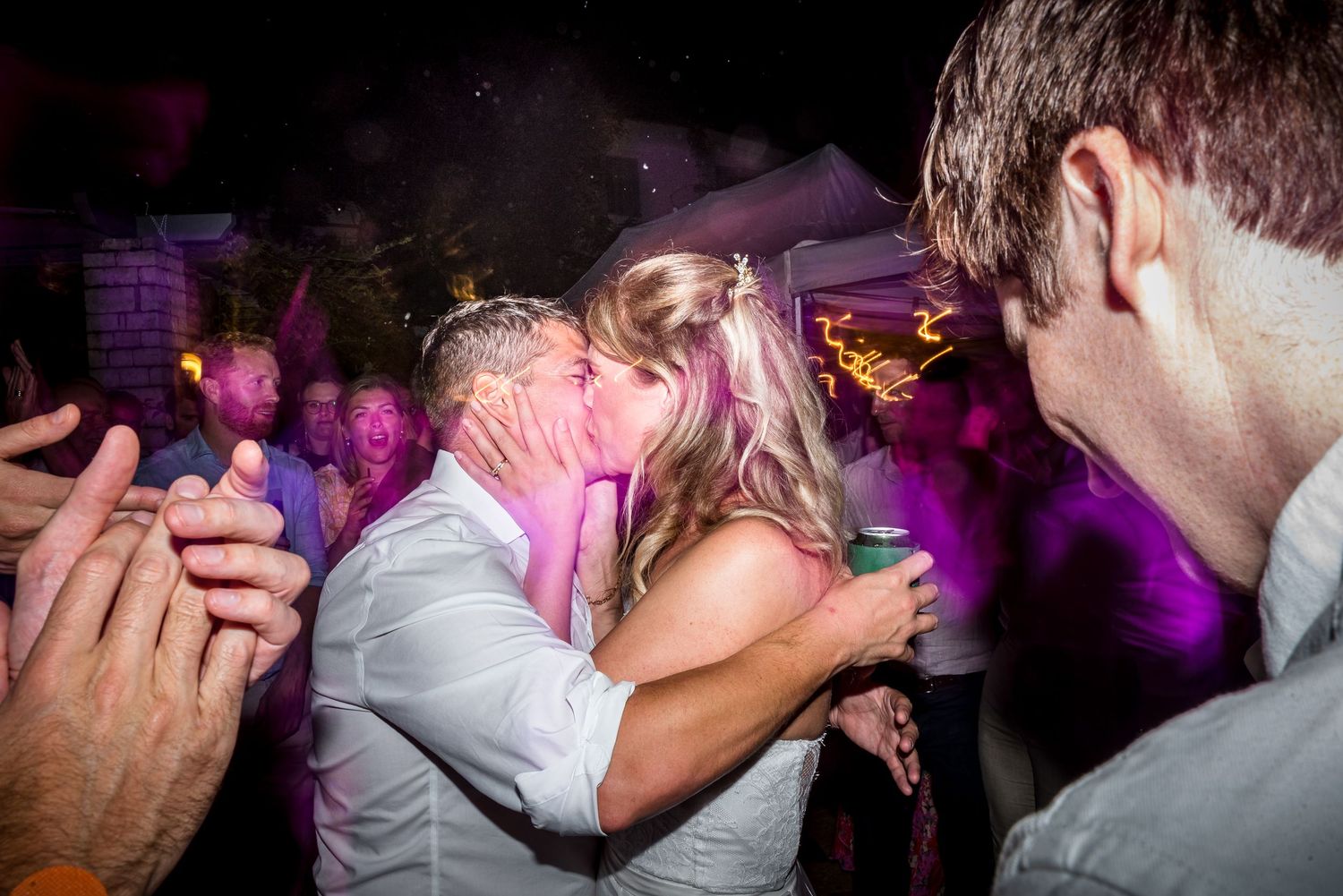 Energetic crowd dancing and celebrating at a nighttime party with purple lighting effects.