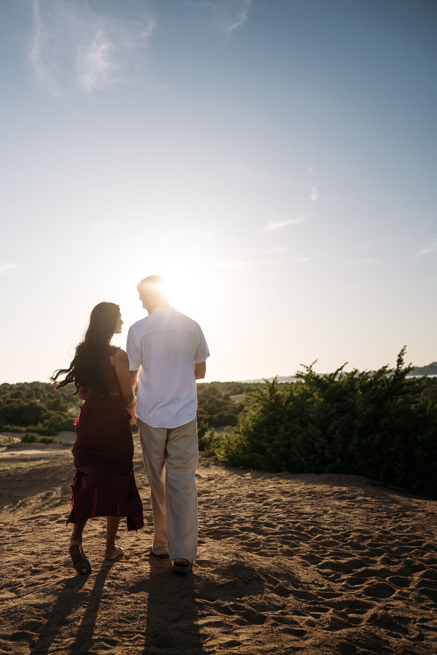 Silhouetted couple walking along a sandy beach path during golden hour.