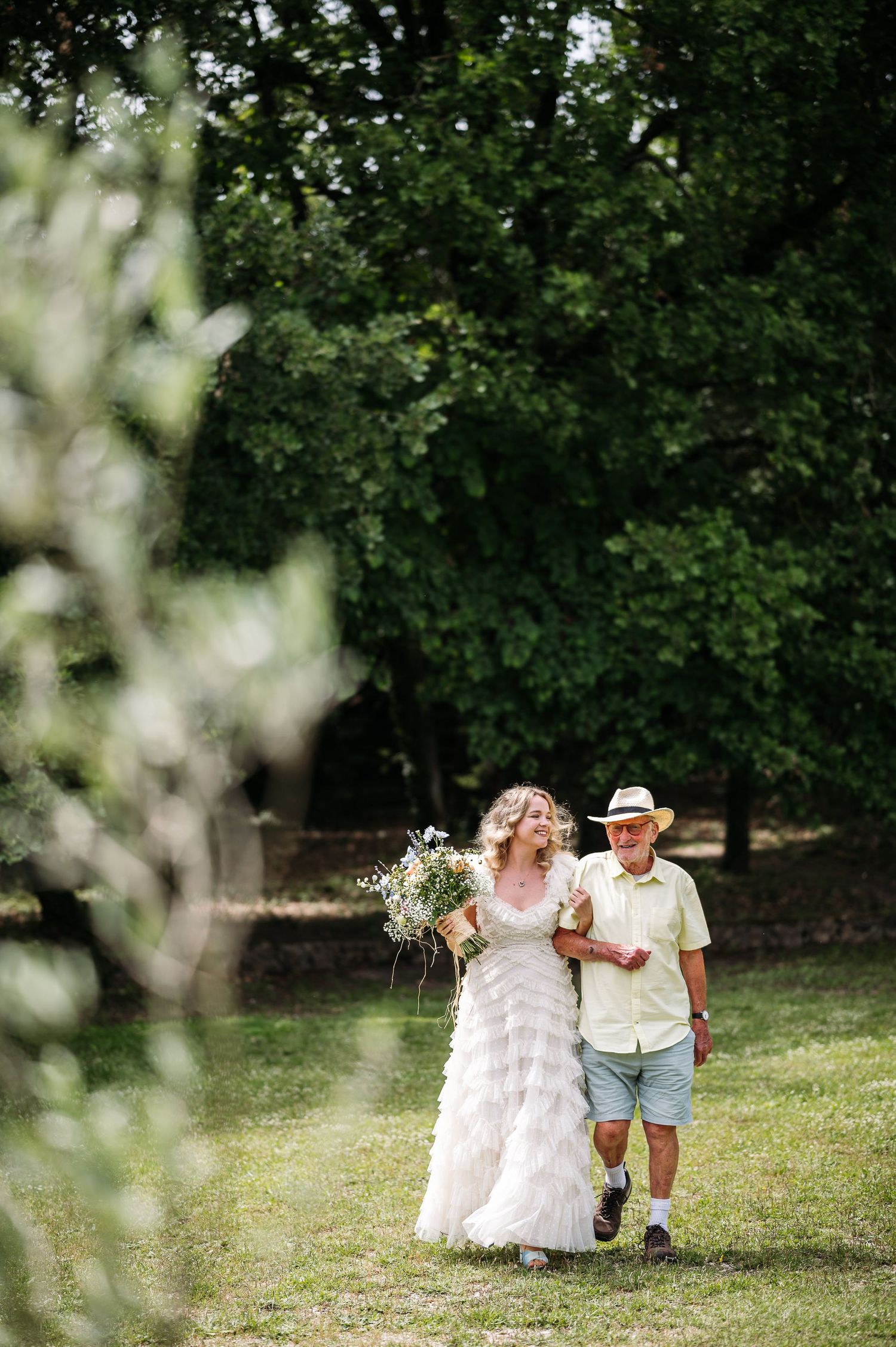 A heartwarming outdoor wedding moment showing two figures walking together through a lush garden setting.
