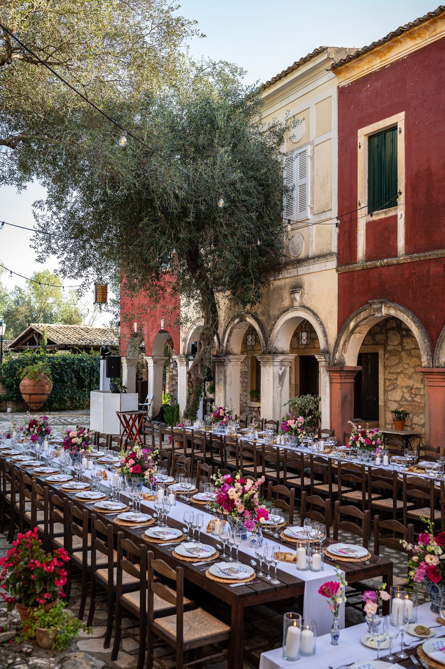 Long dining tables set under Mediterranean arches with pink floral arrangements and white linens.
