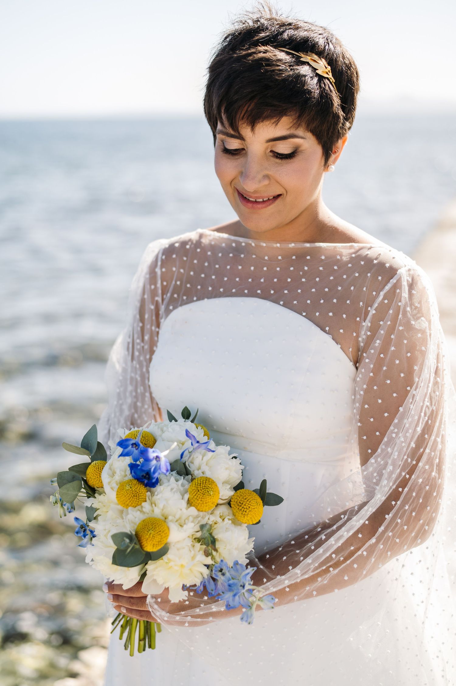 Close-up of a delicate polka dot wedding dress sleeve and yellow and blue bouquet.