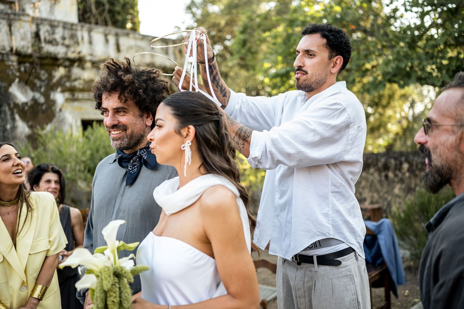 Wedding party members interact during an outdoor garden celebration with natural greenery.