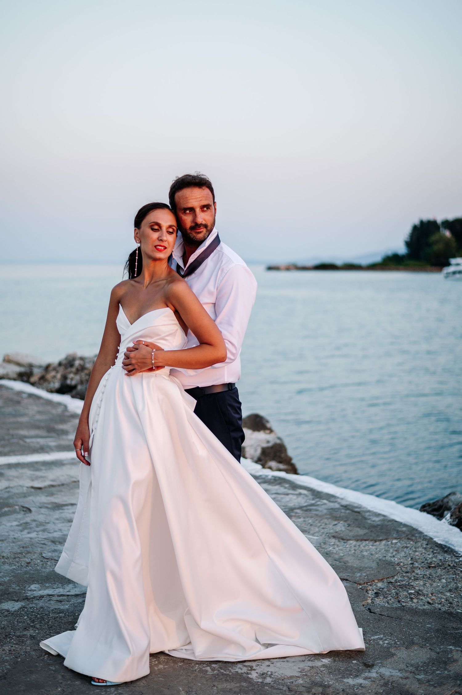 Romantic coastal wedding photos with couple embracing near ocean at dusk.