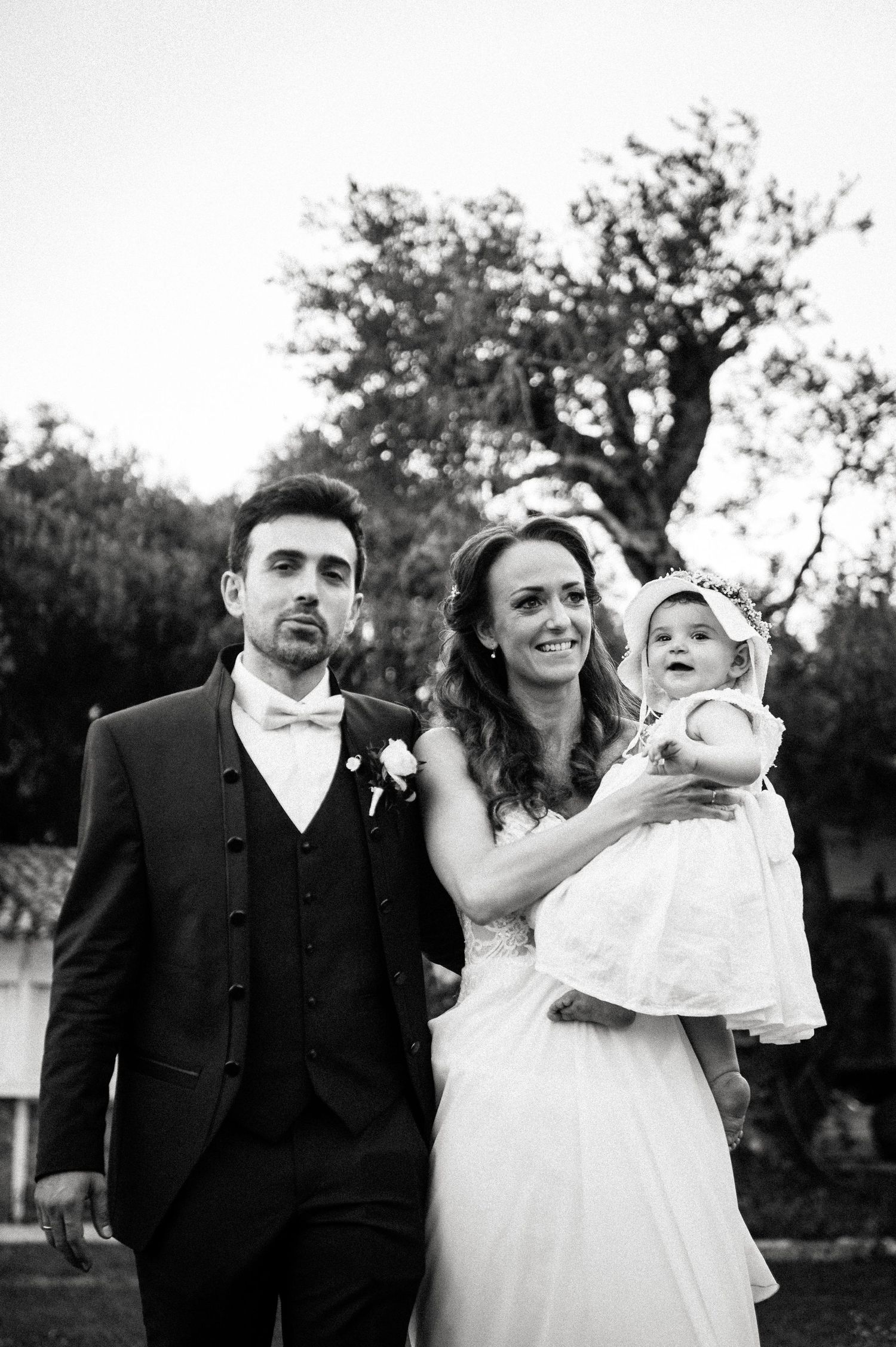 Wedding couple celebrates outdoors with their baby in formal attire.