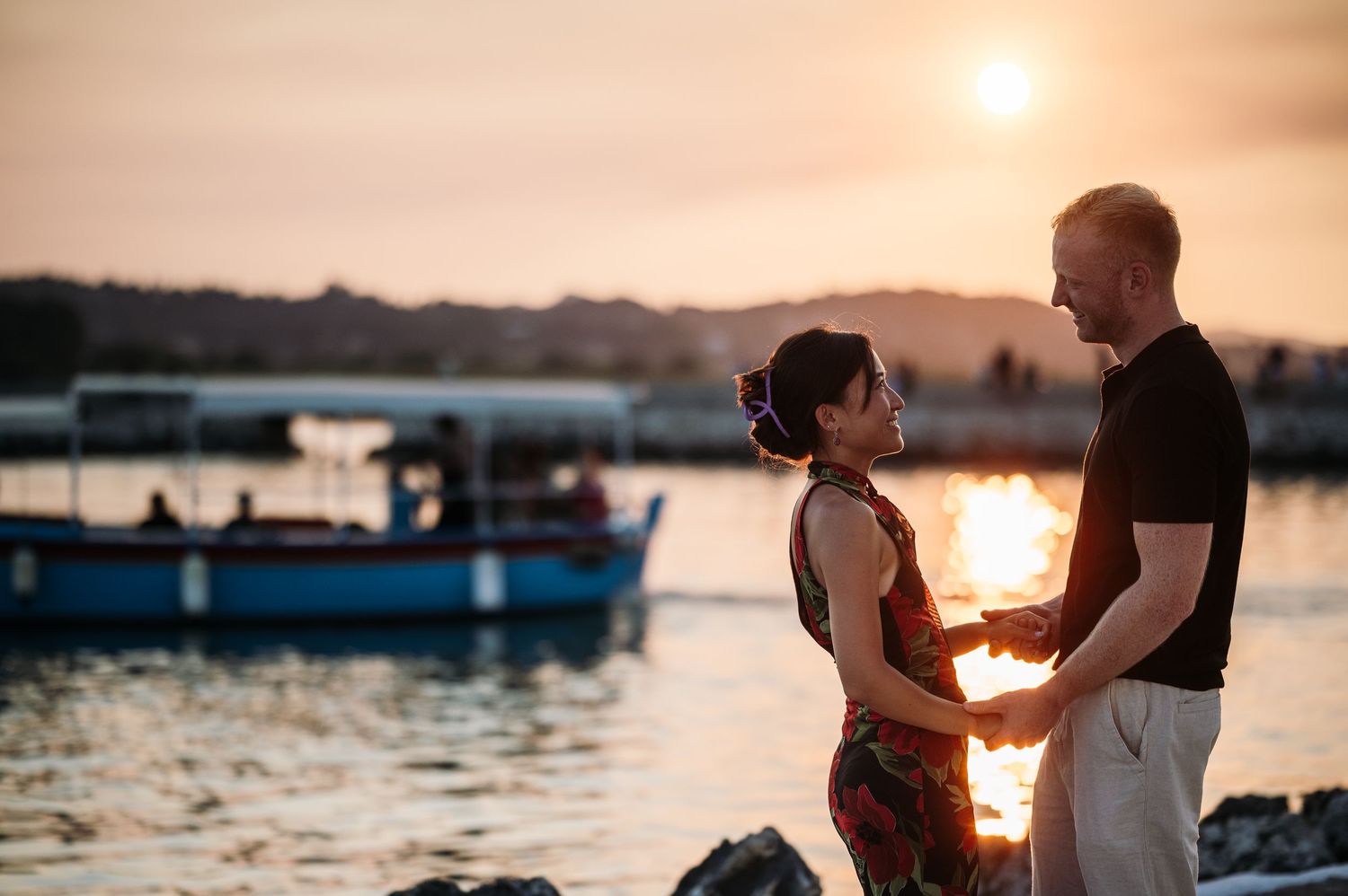 A romantic sunset moment by the harbor with boats in the background.
