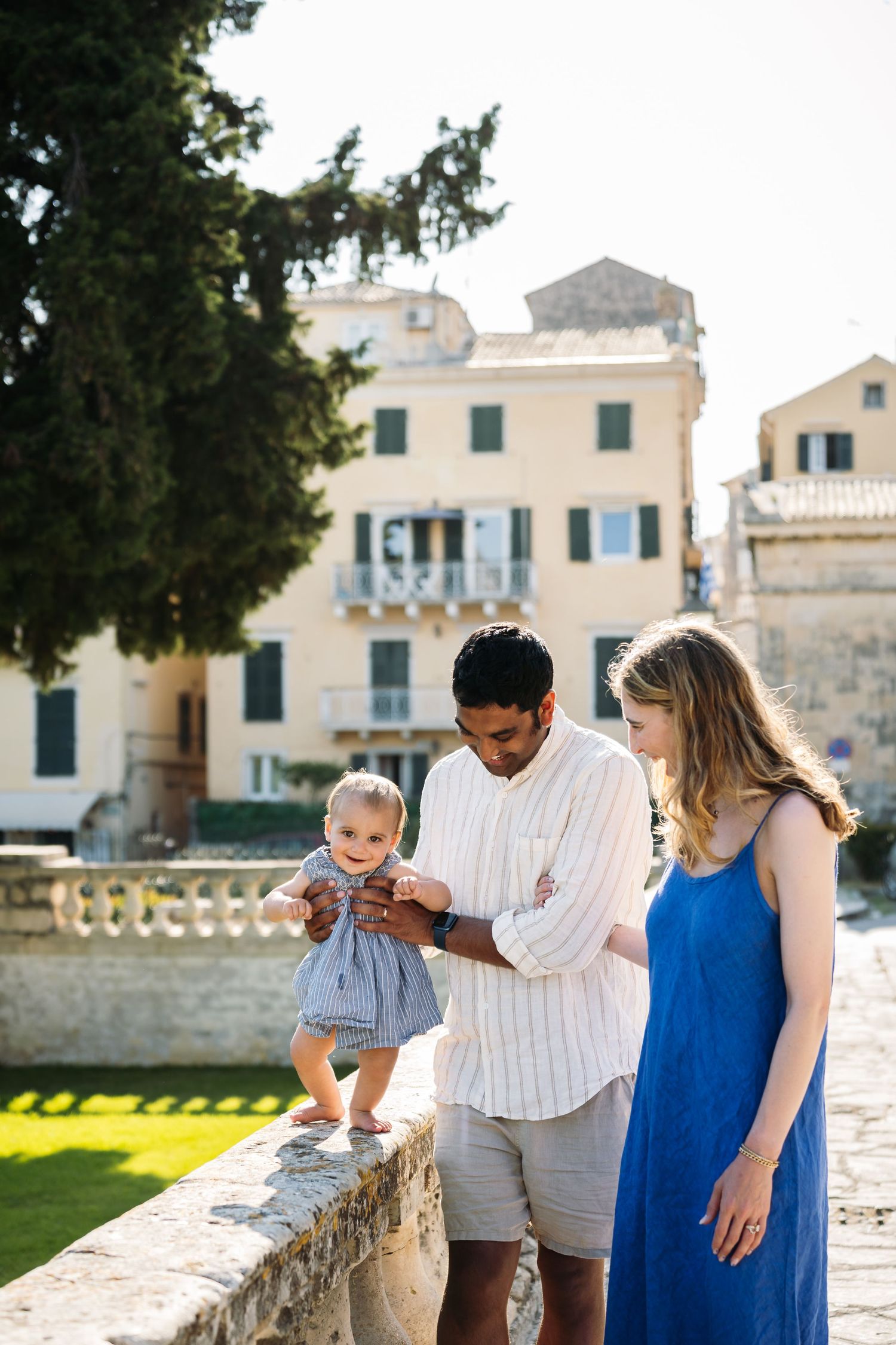 Family enjoying a sunny day together by Mediterranean-style buildings with blue shutters.