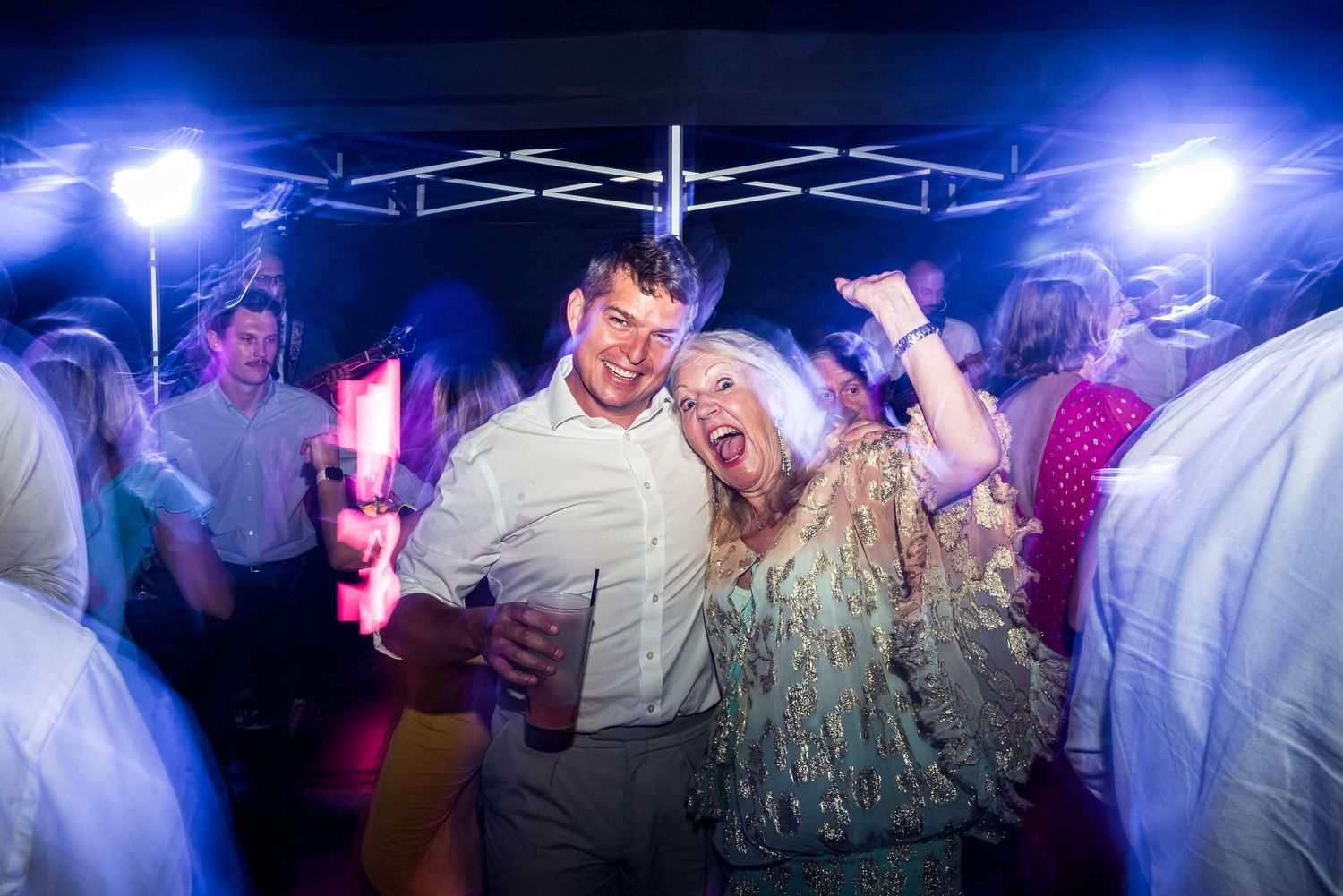 People dancing under bright blue stage lighting at an evening celebration.