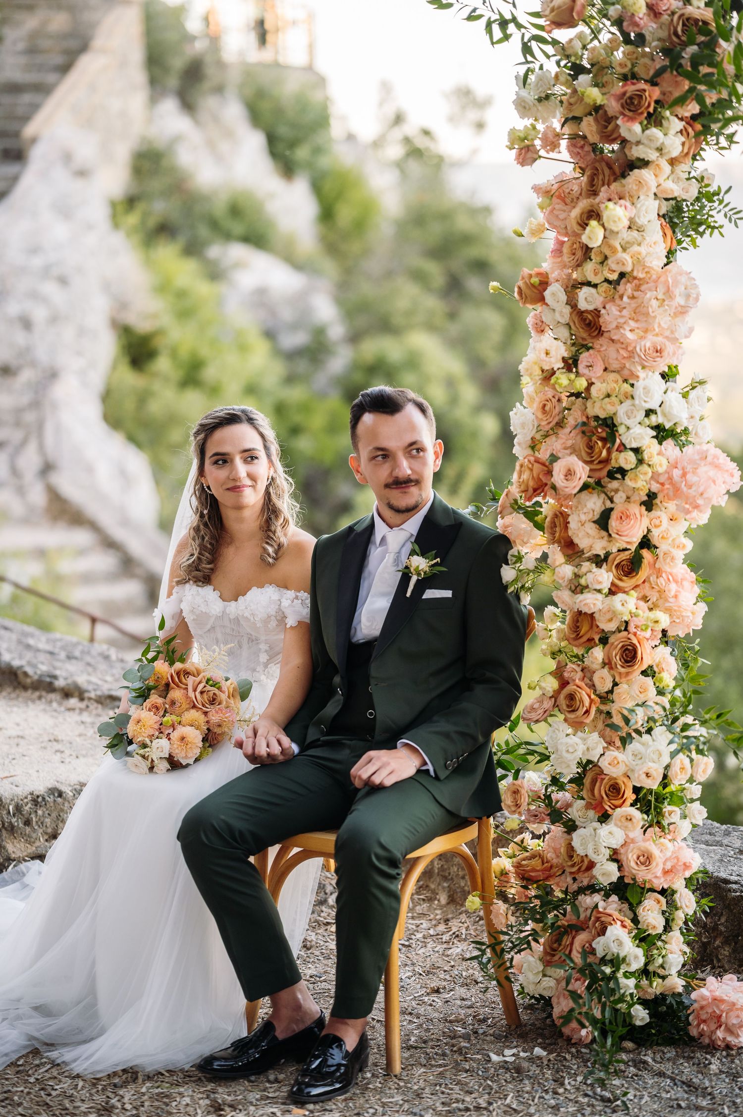 Romantic wedding setting with peach floral arch and rustic stone wall backdrop.