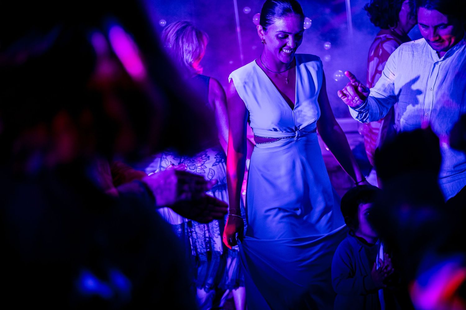 Party crowd dancing under colorful nightclub lights with blue and purple hues.
