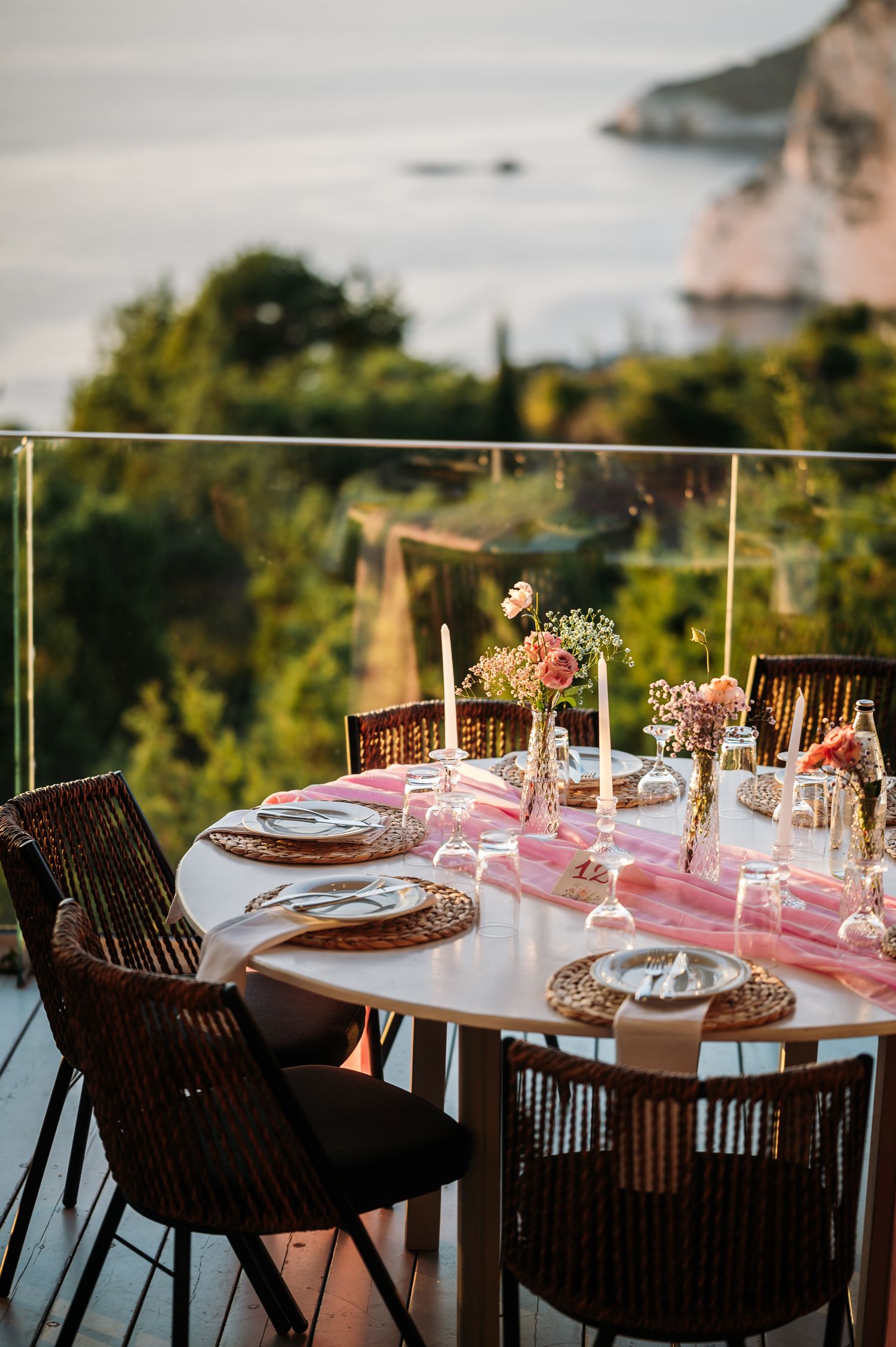 Elegant outdoor dining table setup with pink runner and coastal view in background.