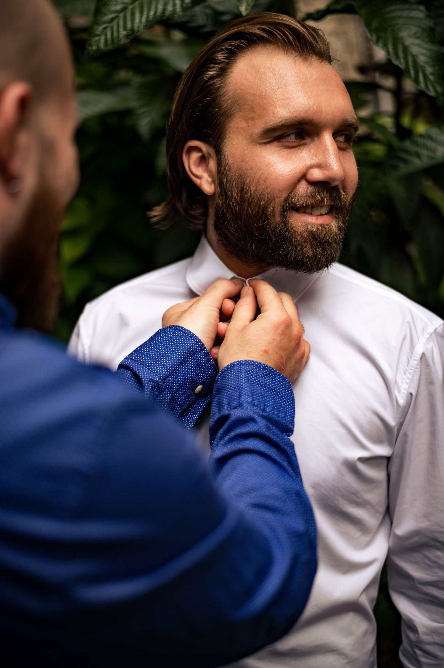 Close-up sequence of someone adjusting a navy blue tie against a natural green backdrop.