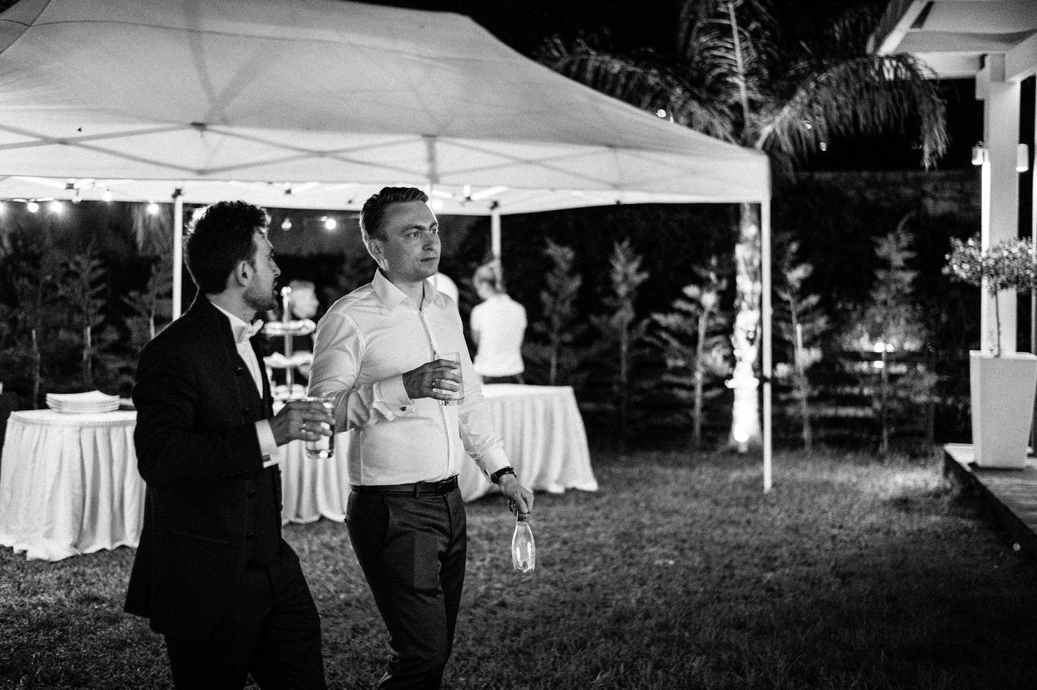 Outdoor wedding tent setup with white tables and chairs on a grassy lawn.