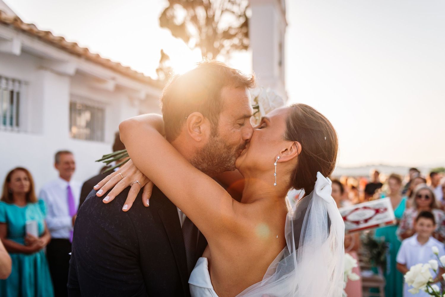 Wedding celebration scene with guests dancing and embracing during sunset.