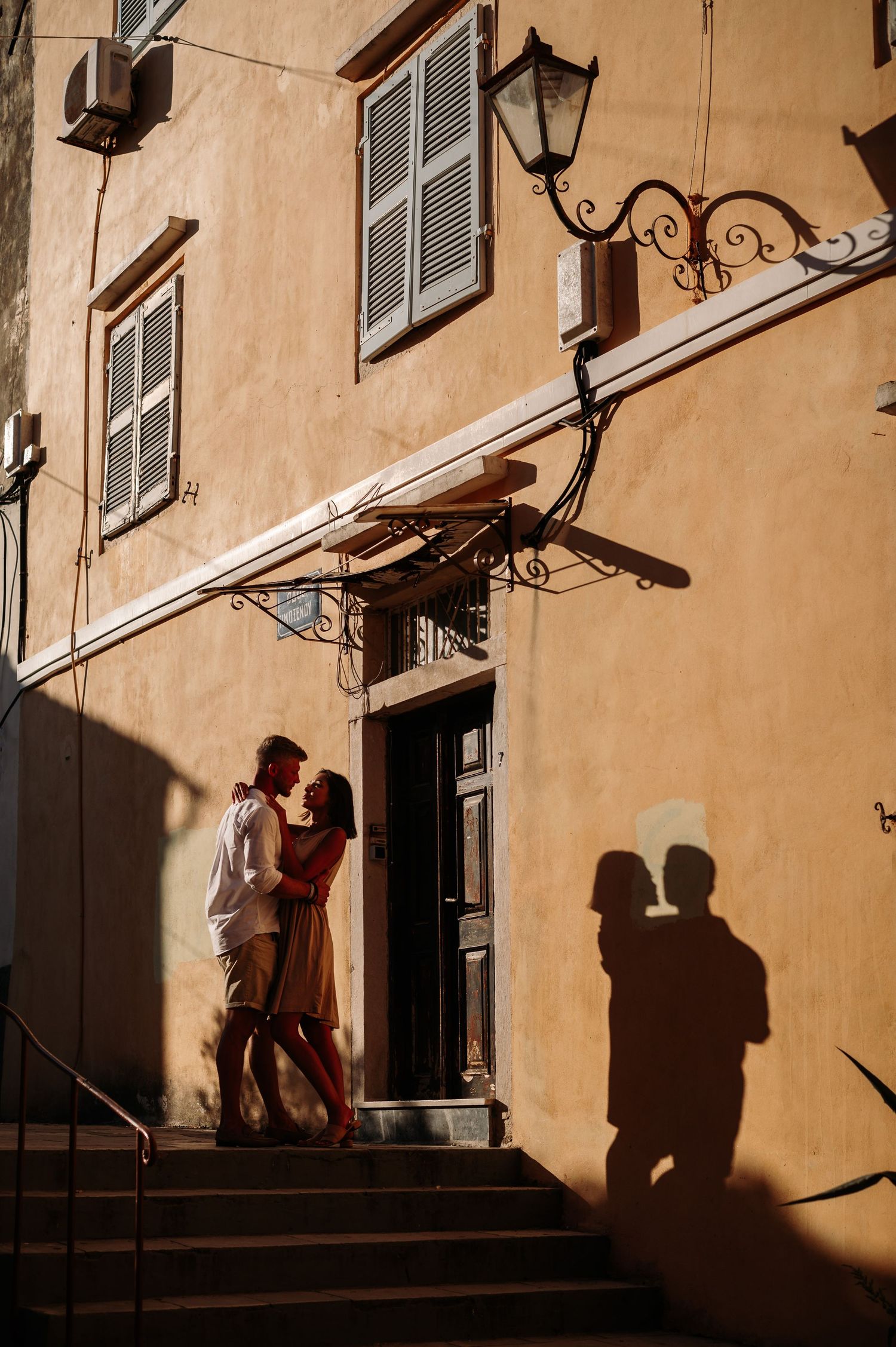 Silhouettes of a couple dancing and embracing against warm-toned building walls at sunset.