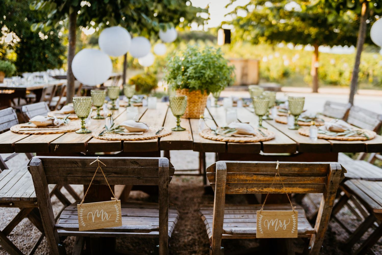 Rustic wooden tables decorated for an outdoor wedding reception with place settings and floral arrangements.