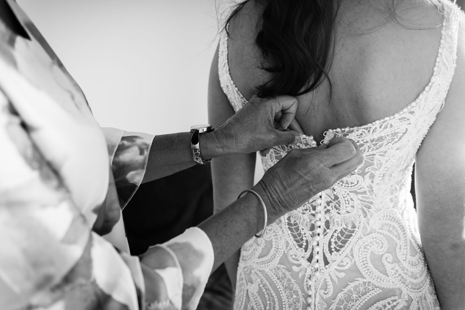 Close-up black and white photo of someone helping with dress buttons.