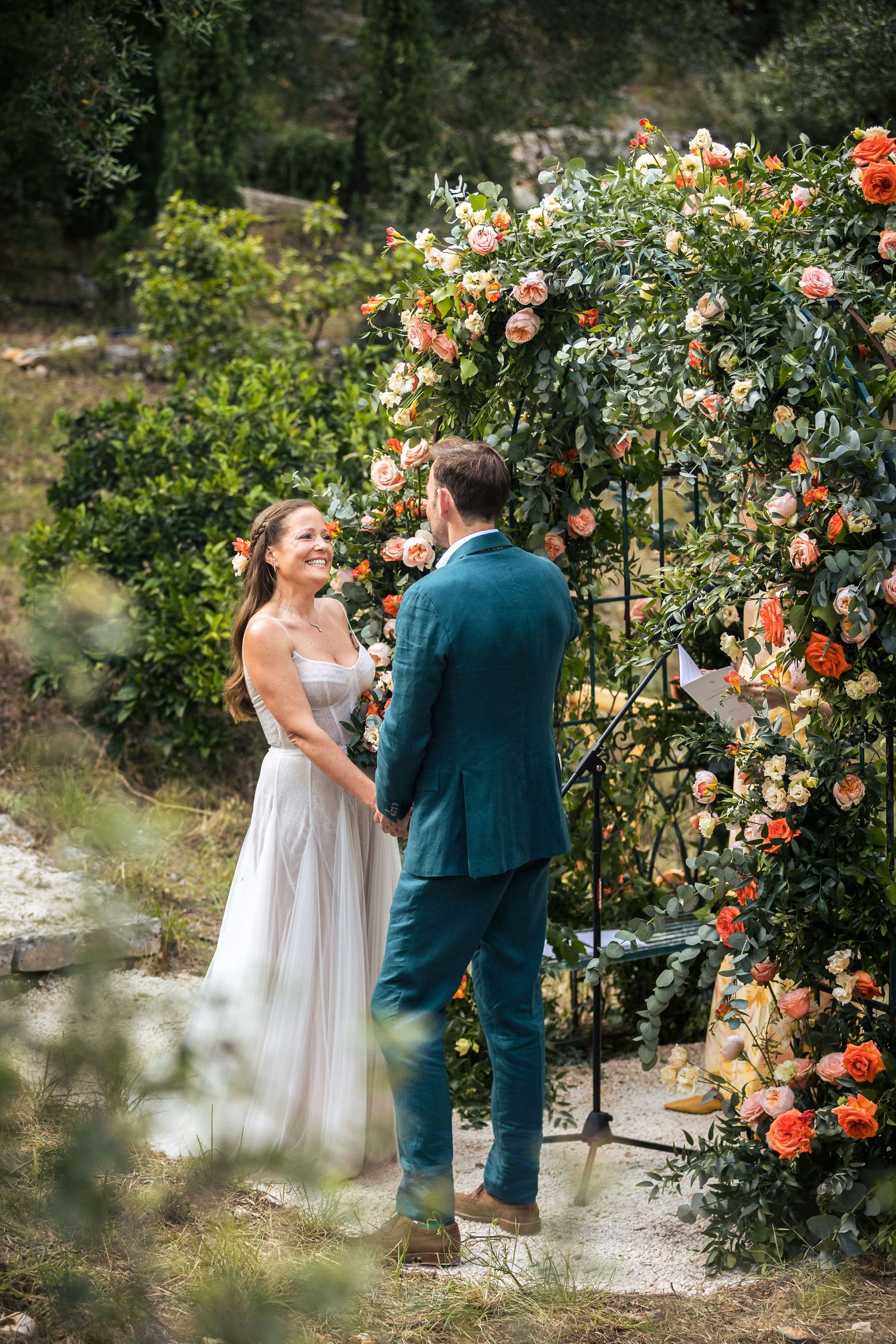 Wedding ceremony moment captured in a garden with blooming coral roses and greenery.