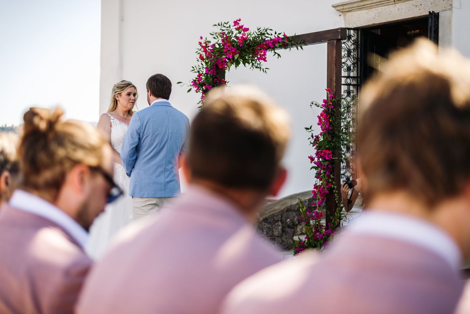 Wedding ceremony arch decorated with pink flowers against white building.