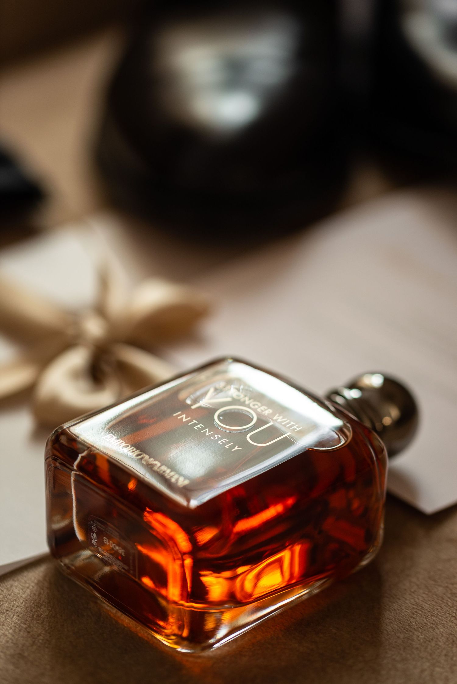 A square glass bottle of amber-colored perfume or cologne on a textured surface.