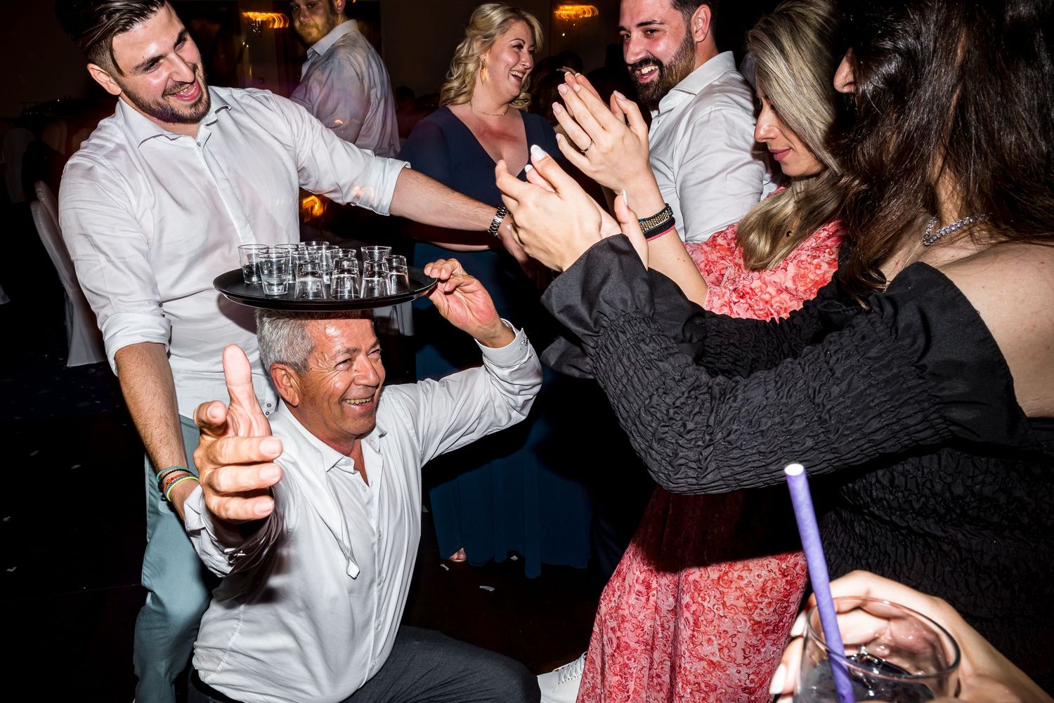 Wedding guests dancing and celebrating enthusiastically on a dark dance floor at a reception party.