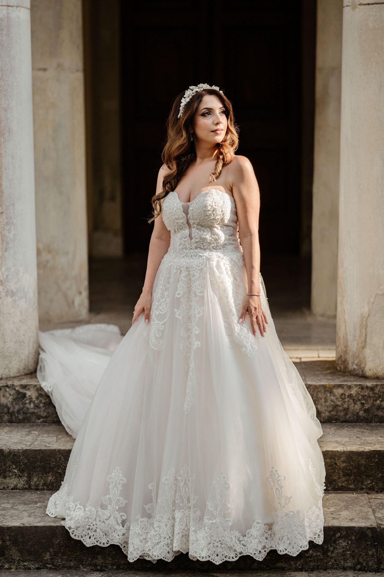 Elegant bride in lace wedding gown posing in front of classical stone columns.
