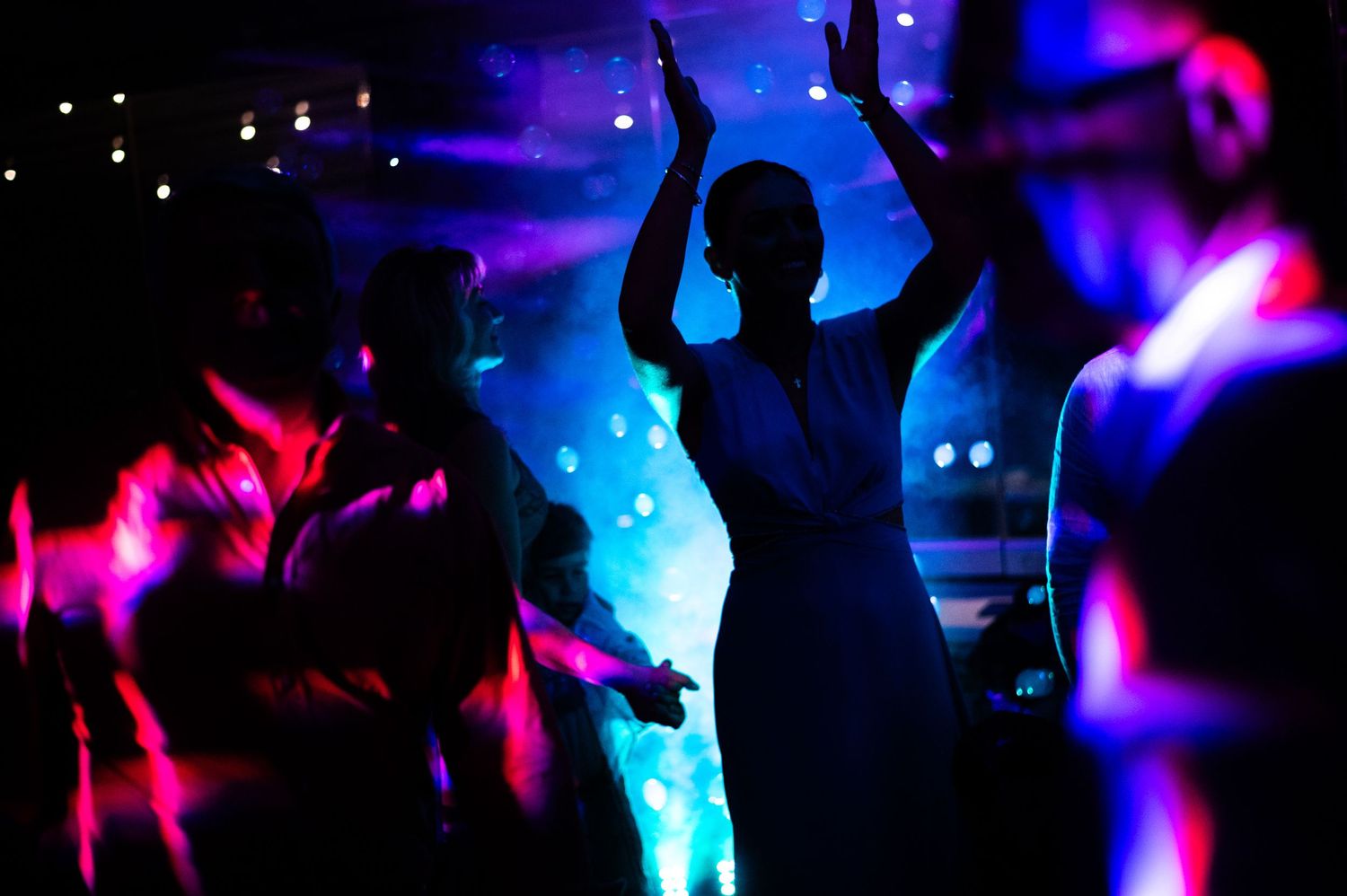 Silhouettes of people dancing at a nightclub with vibrant blue and pink lighting effects.