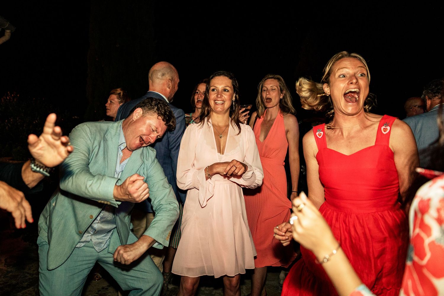 Wedding guests dancing enthusiastically under dramatic lighting at night.